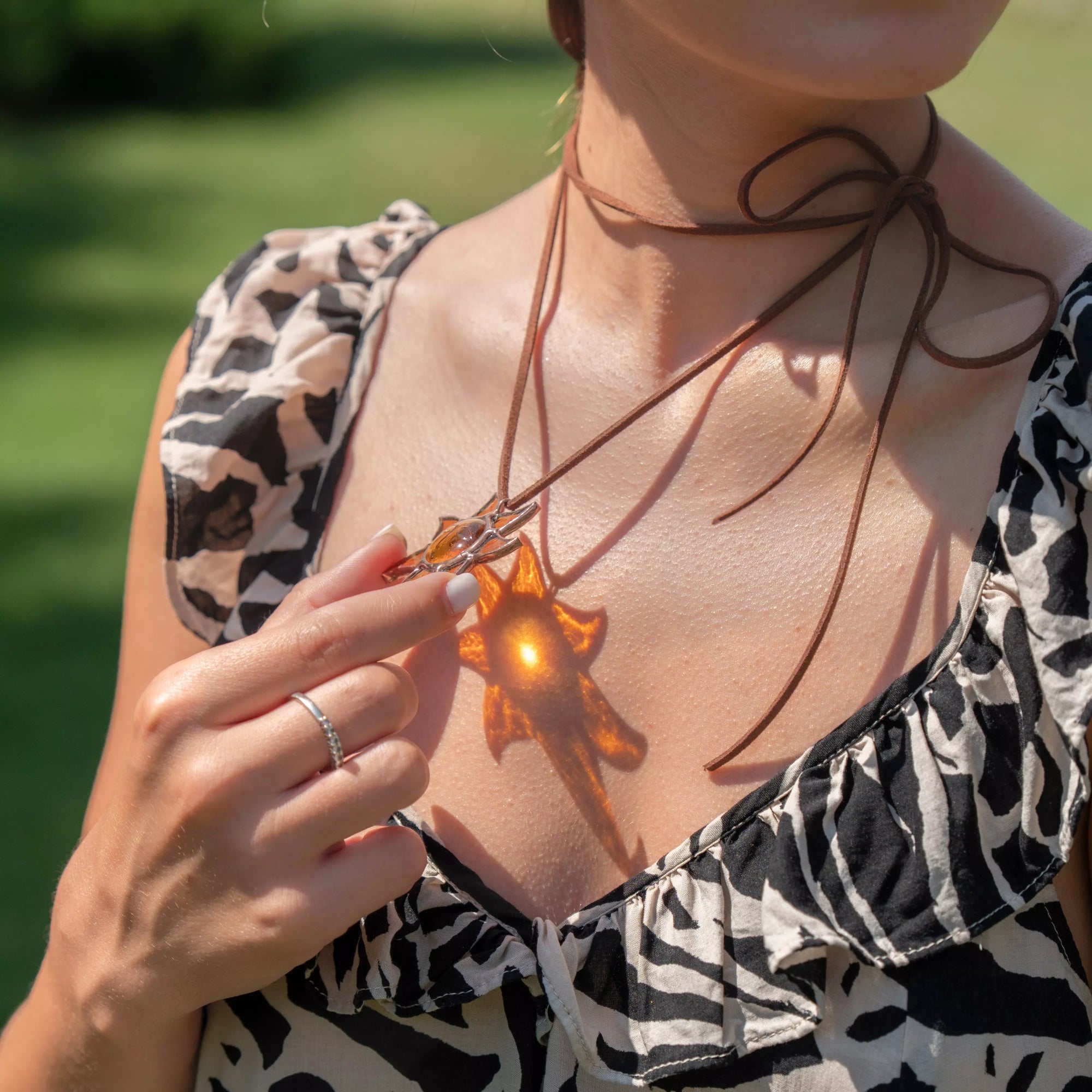 Woman holding stained glass sun pendant with glowing reflection on chest in natural sunlight
