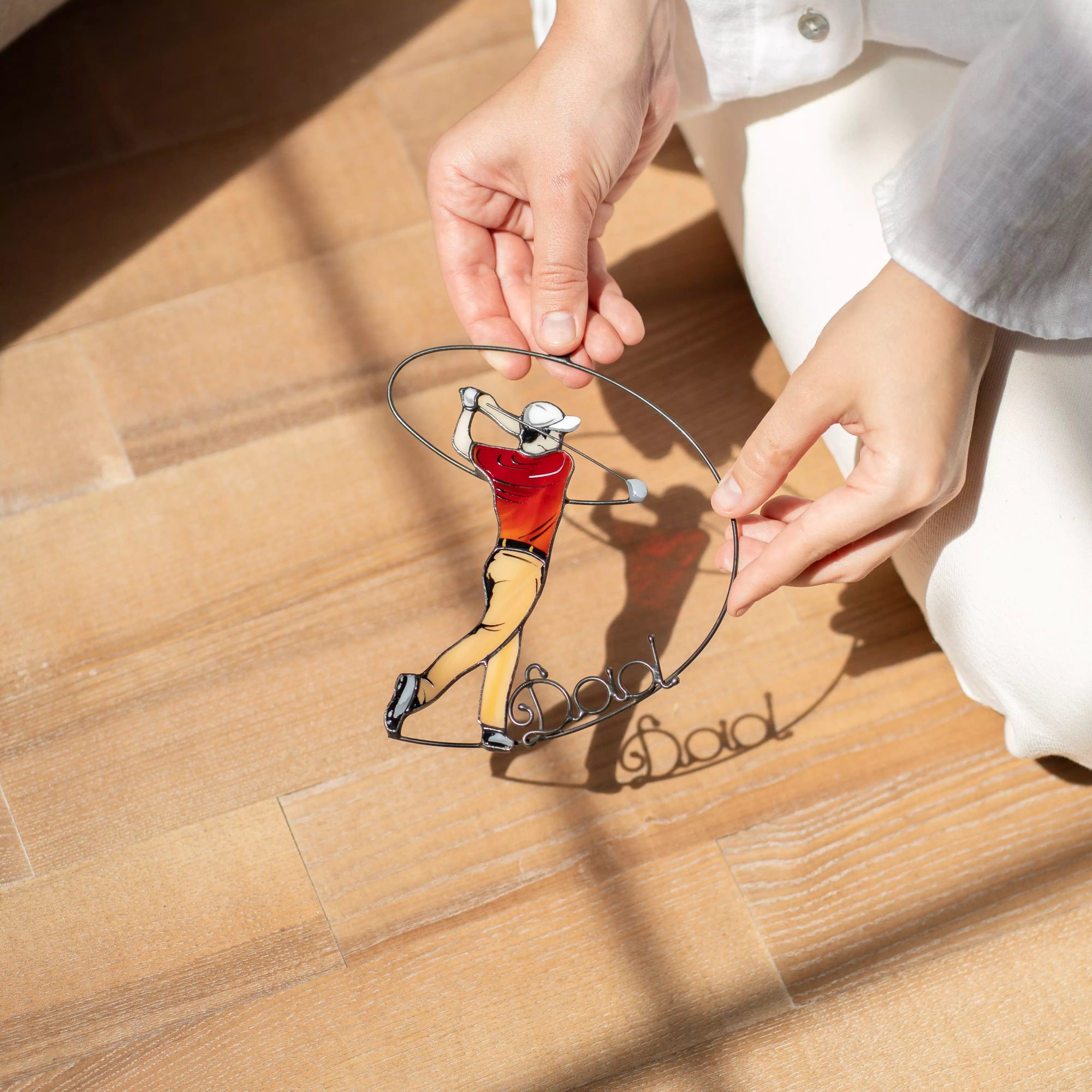 Stained glass ornament with a golfer design and 'Best Dad' text on a wooden surface.