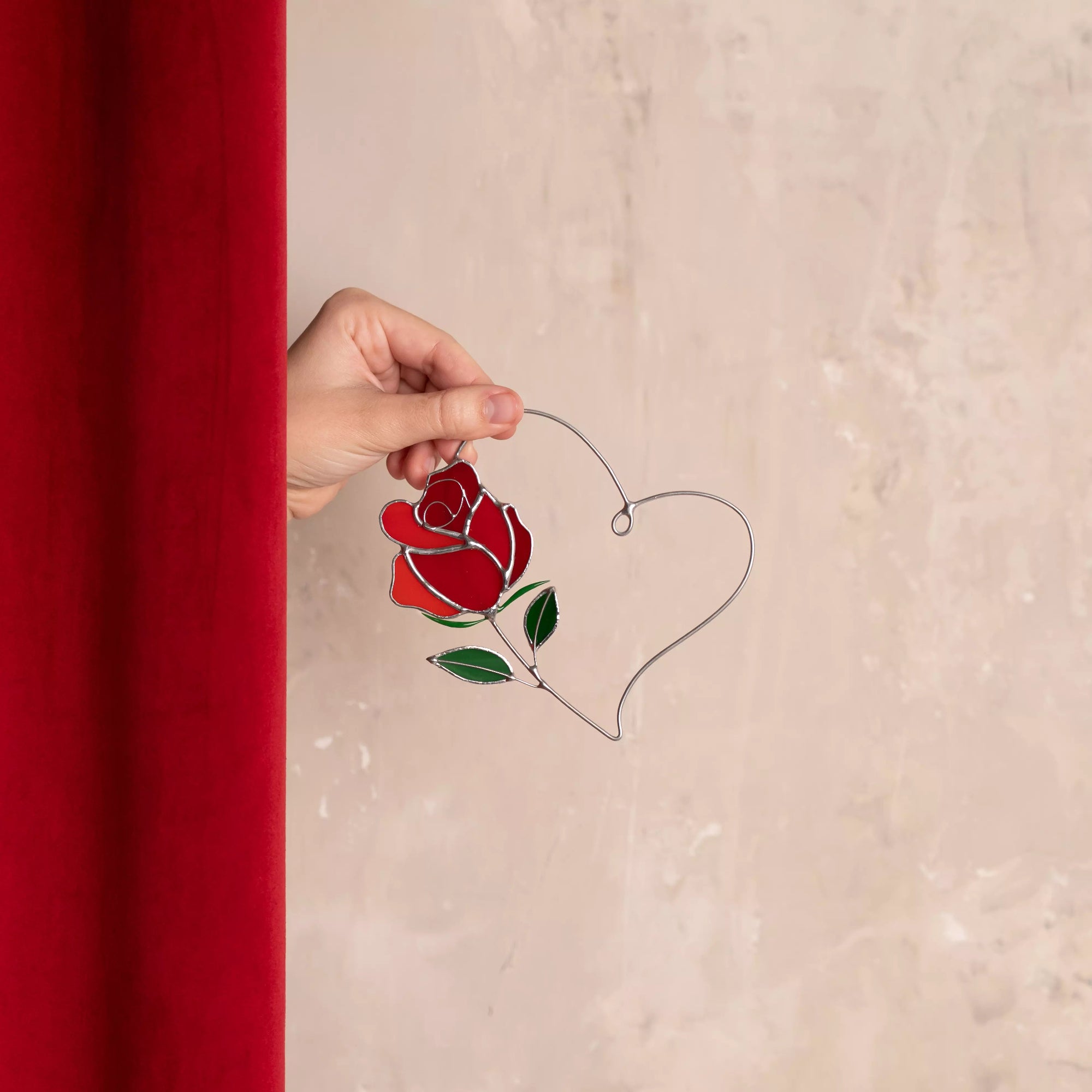 Rose heart stained glass suncatcher held in one hand to show size and delicate craftsmanship.