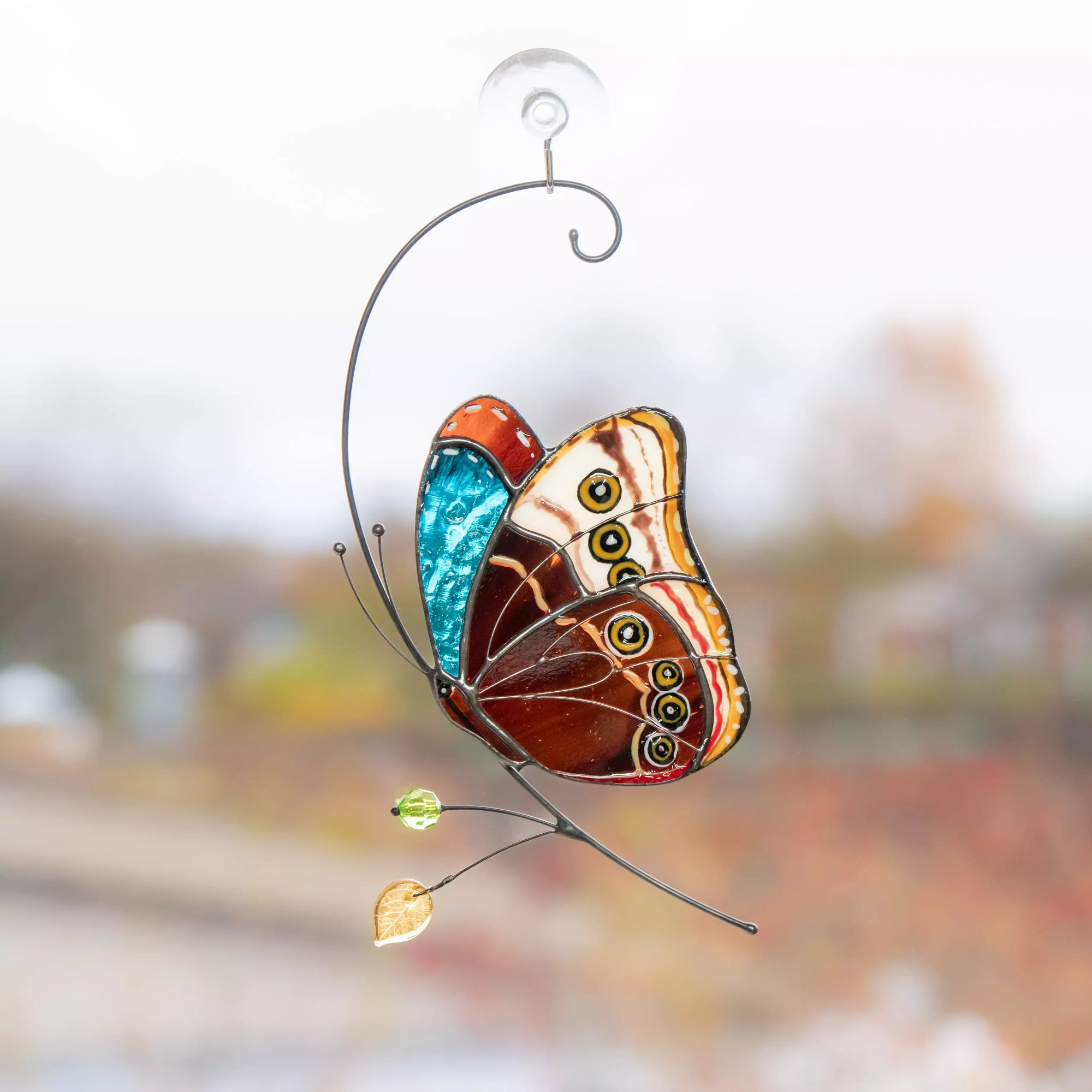 Stained glass butterfly with blue and orange wings hanging on window with suction cup