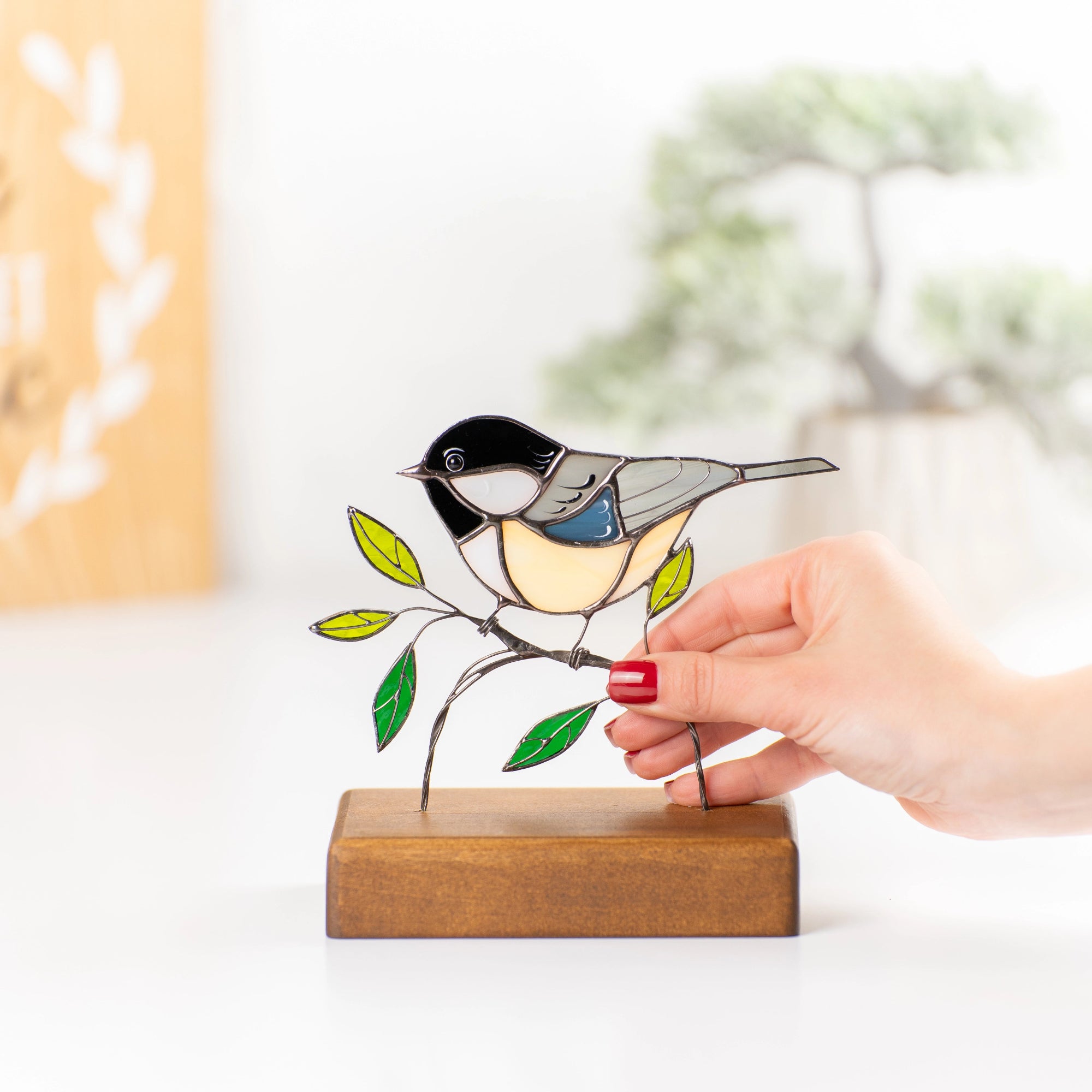 Hand holding chickadee stained glass bird with colorful green leaves and soft yellow tones