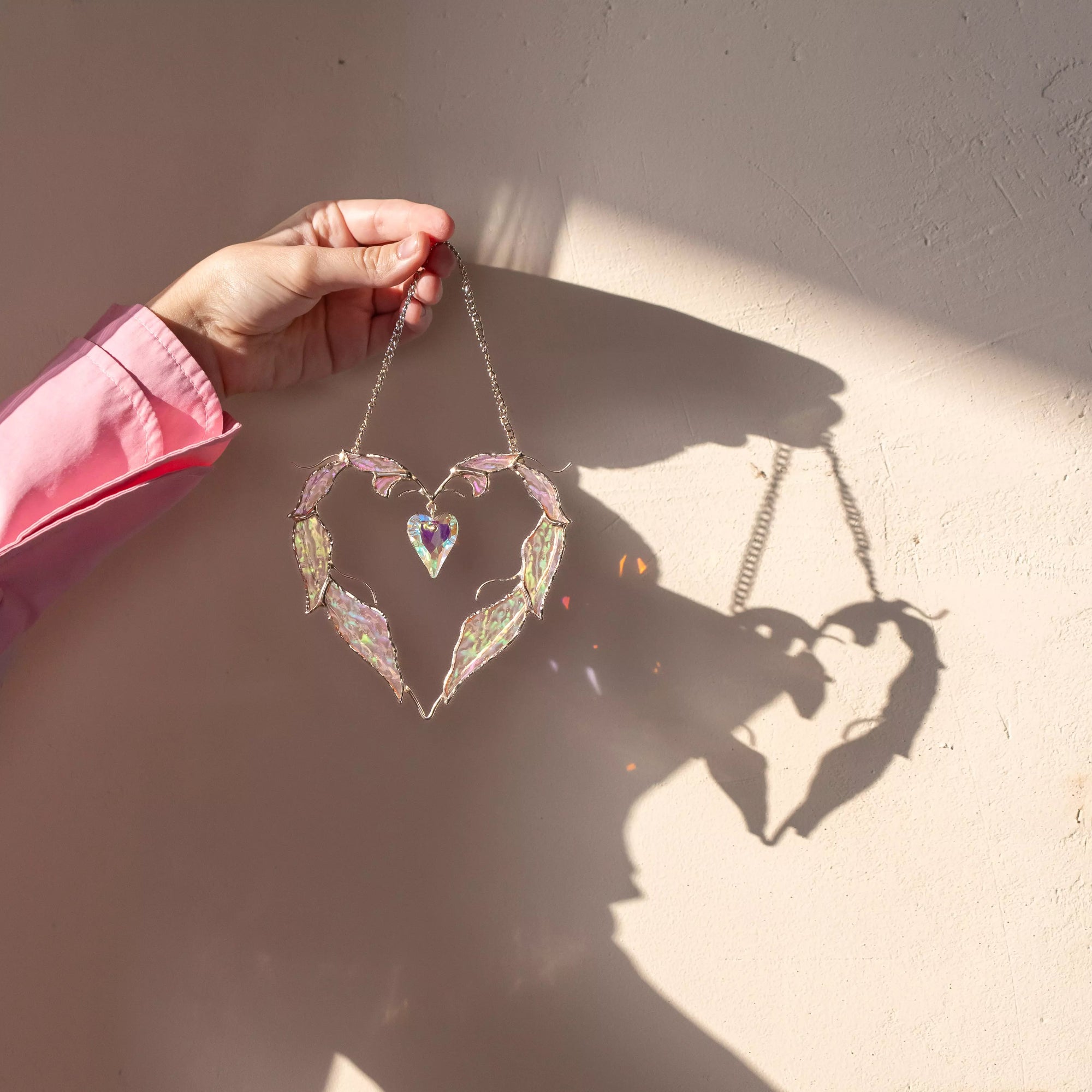 This handmade stained glass window hanging features iridescent feathers and a crystal heart, offering a delicate yet eye-catching romantic decor piece.