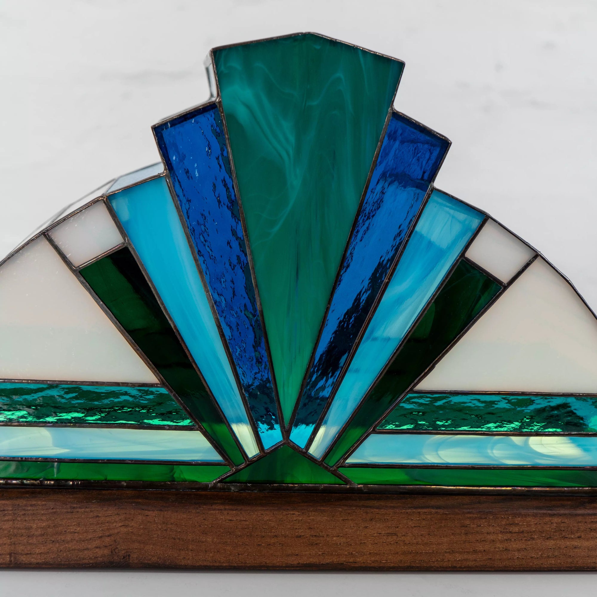 Close-up of handmade blue stained glass lamp, featuring teal and aqua glass textures on a natural wood base.
