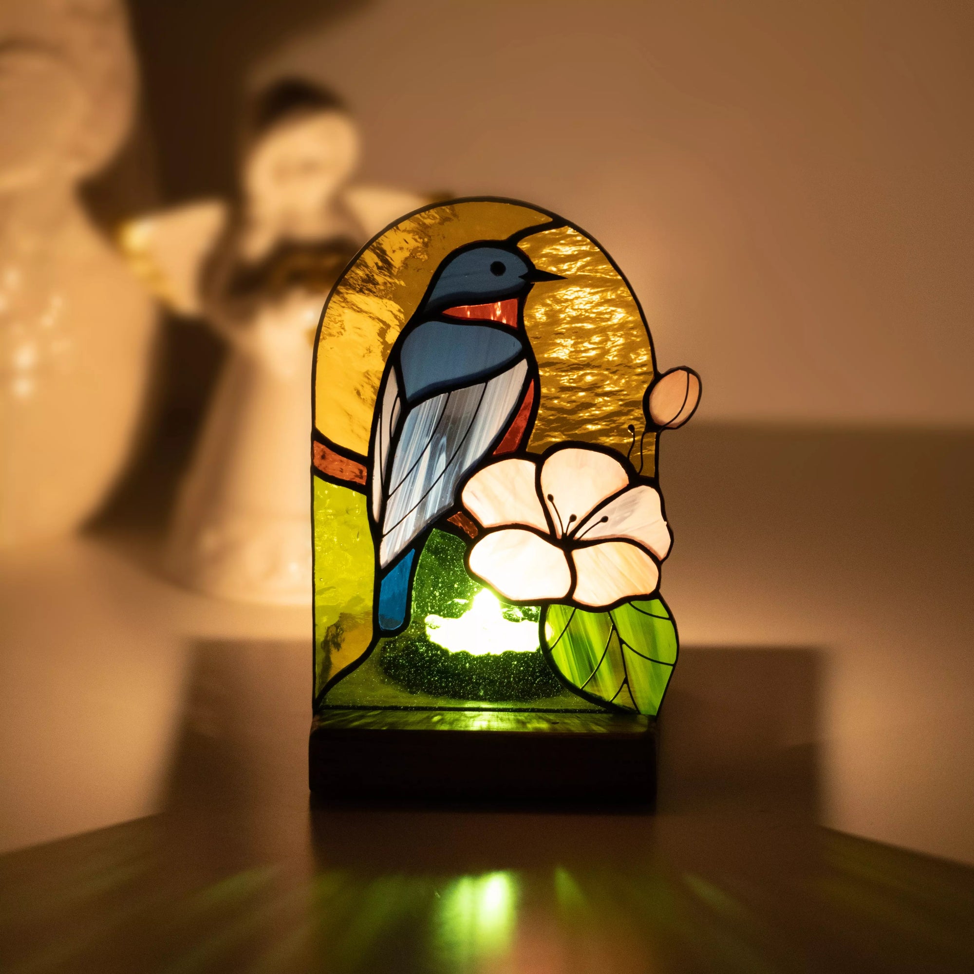 Angled view of stained glass lamp with blue and orange bird, soft lighting in background