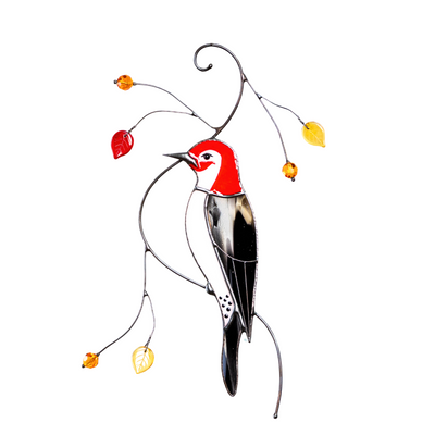 Stained glass woodpecker suncatcher hanging indoors with curved wire branches and red, orange, and yellow glass leaves.