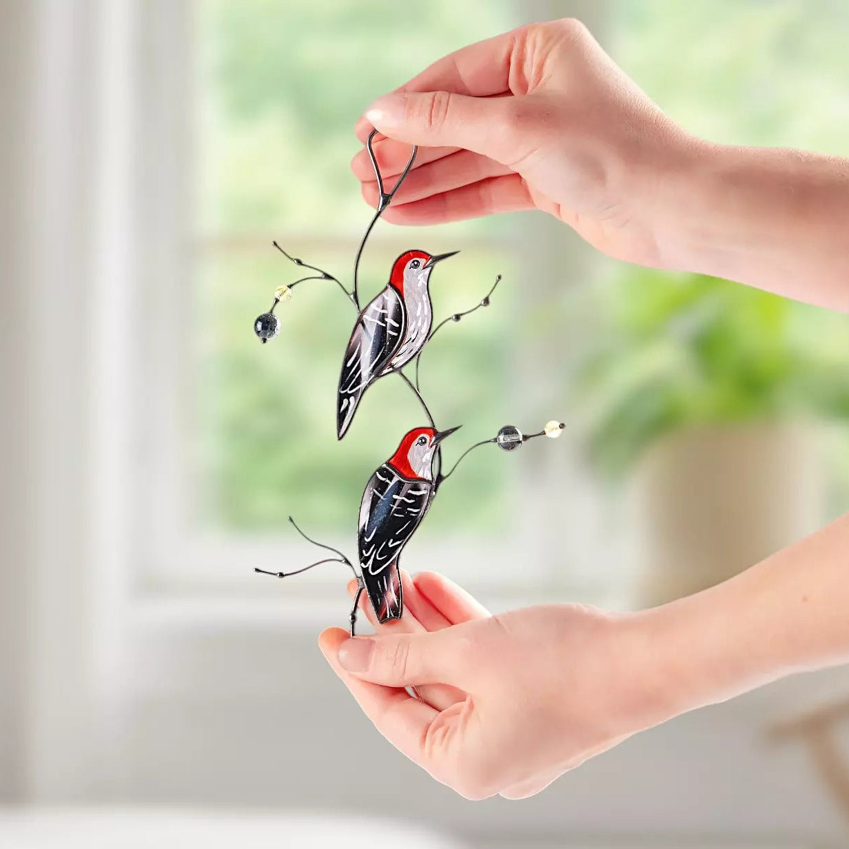 A person's hands holding the woodpecker suncatcher against a bright indoor background, demonstrating the scale of the piece.
