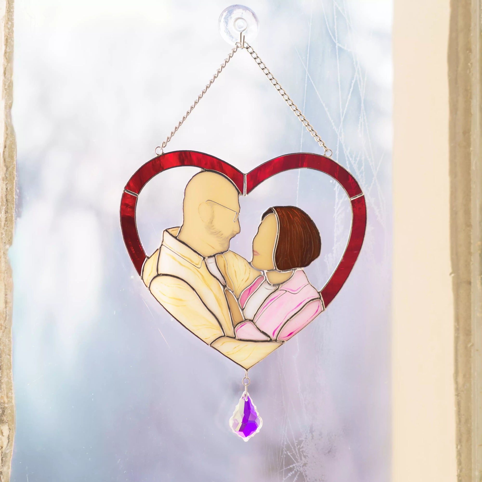 Heart-shaped stained glass panel with a couple embracing, hanging against a light background.