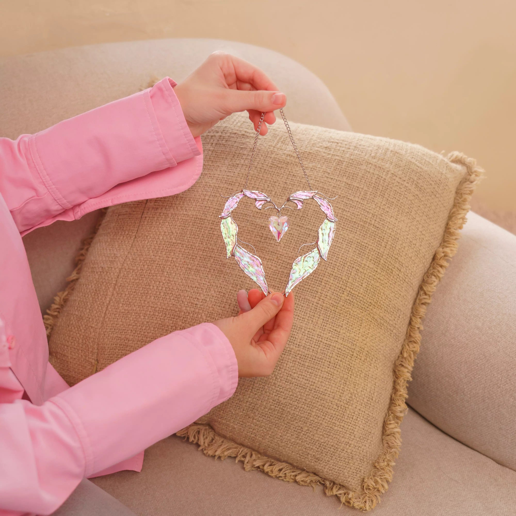 Close-up view of a love stained glass heart suncatcher showing iridescent glass feathers, solder lines, and a faceted crystal heart.