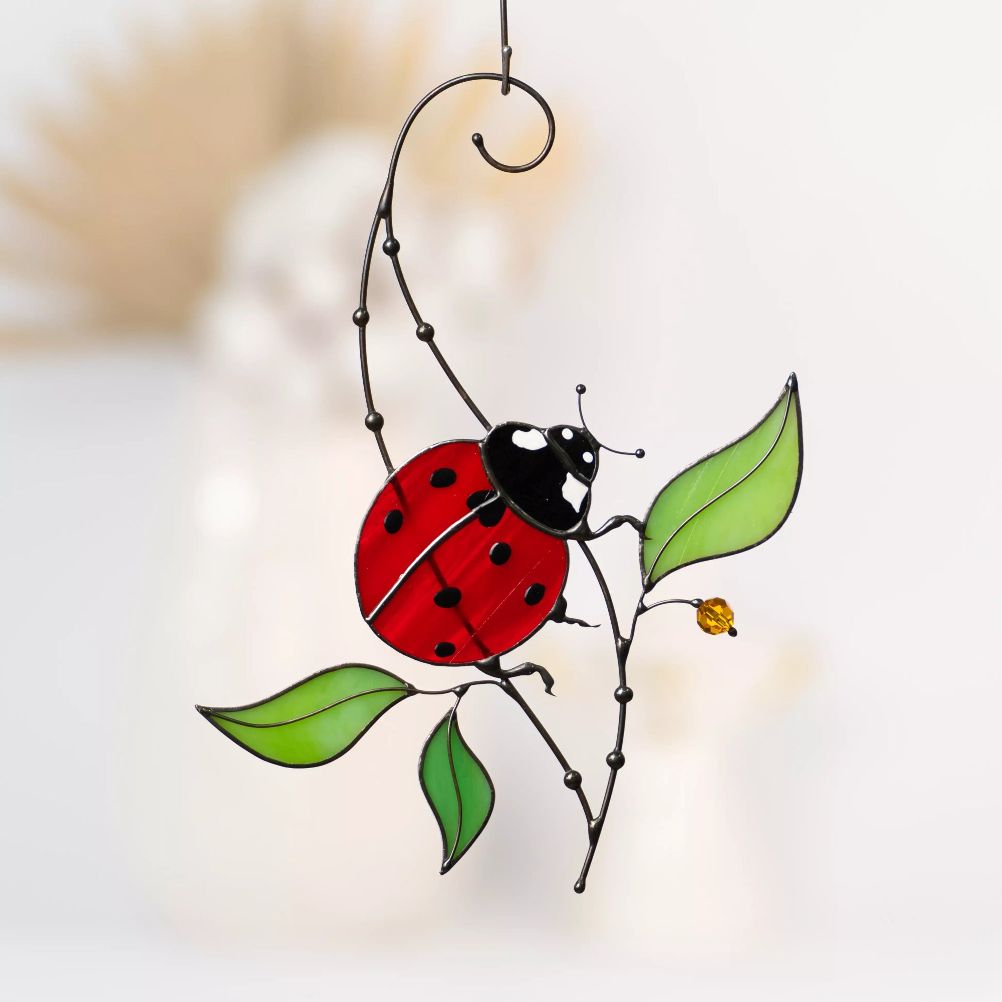 Close-up view of a stained glass ladybug suncatcher with red wings, black spots, and green leaves on a metal frame with a yellow crystal flower.