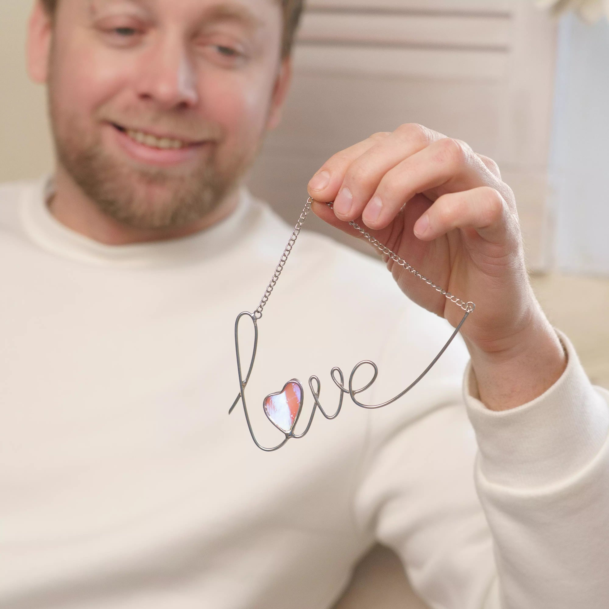 Lifestyle photo of a love stained glass wire sign held by a person, showing a silver wire word and iridescent pink heart.