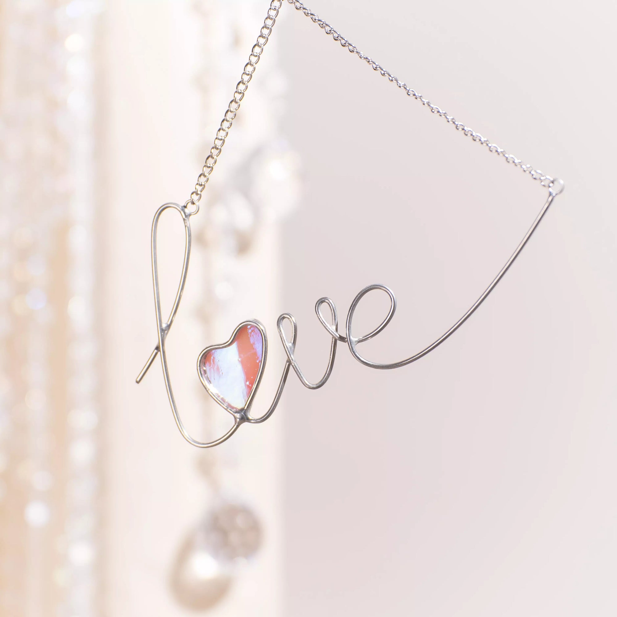Love stained glass wire sign hanging on a window using a suction cup, featuring a soft pink iridescent glass heart.