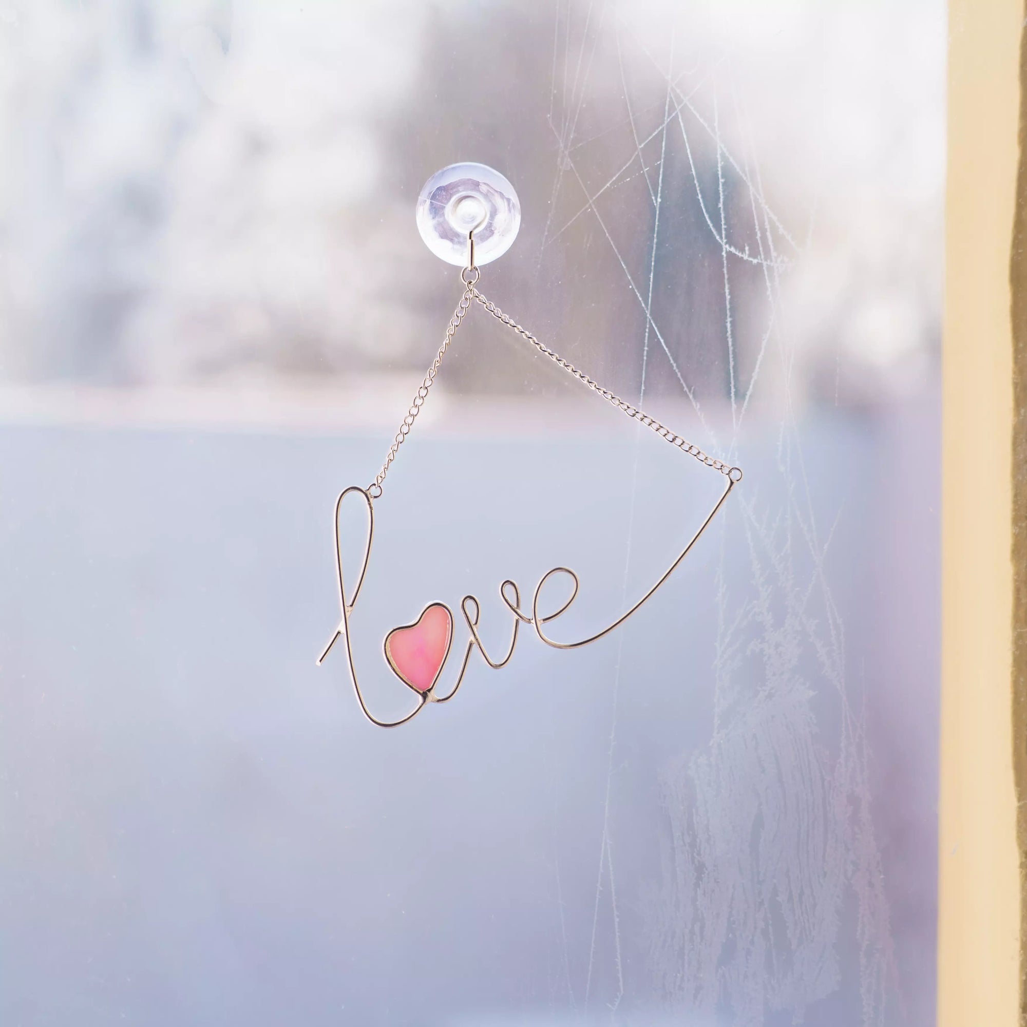 Love stained glass wire sign hanging on a window using a suction cup, featuring a soft pink iridescent glass heart.