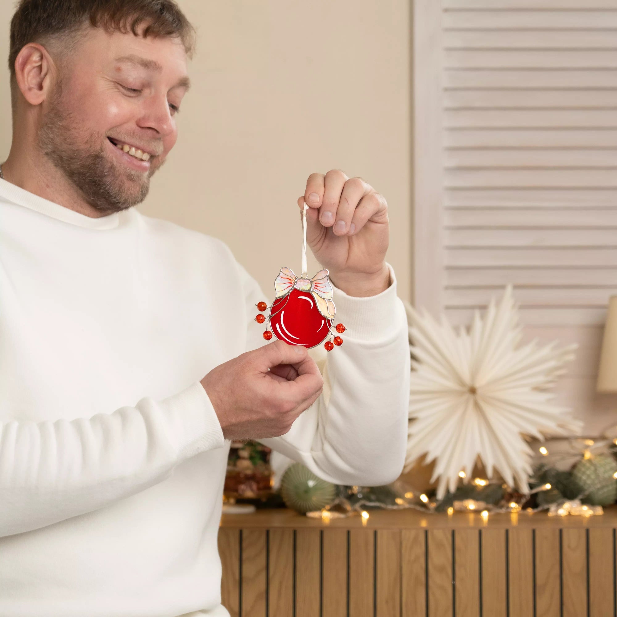 Man holding a red Christmas stained glass ornament in a festive interior design
