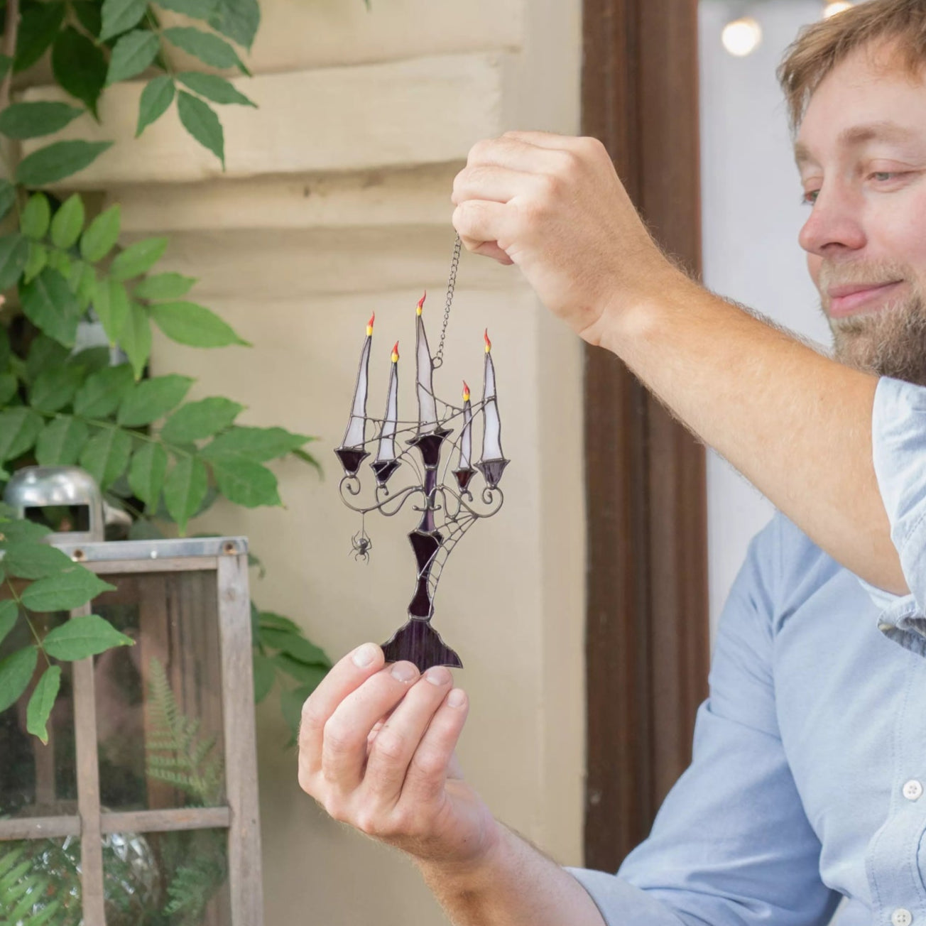 Man holding a small decorative candelabra suncatcher outdoors with plants and lanterns in the background