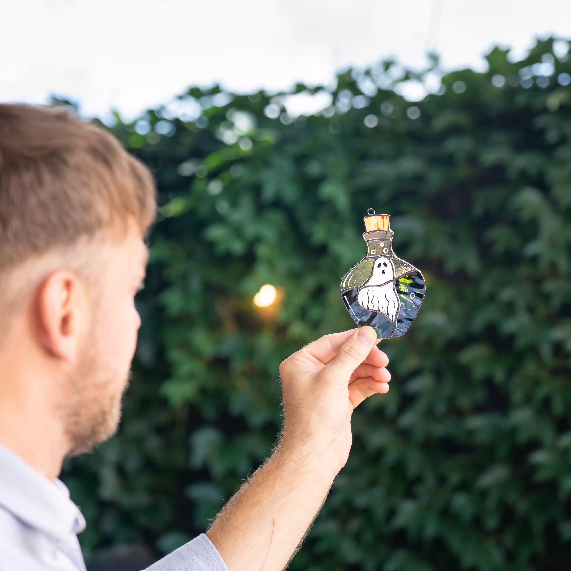 Man holding stained glass decorative halloween suncatcher with a ghost design outdoors