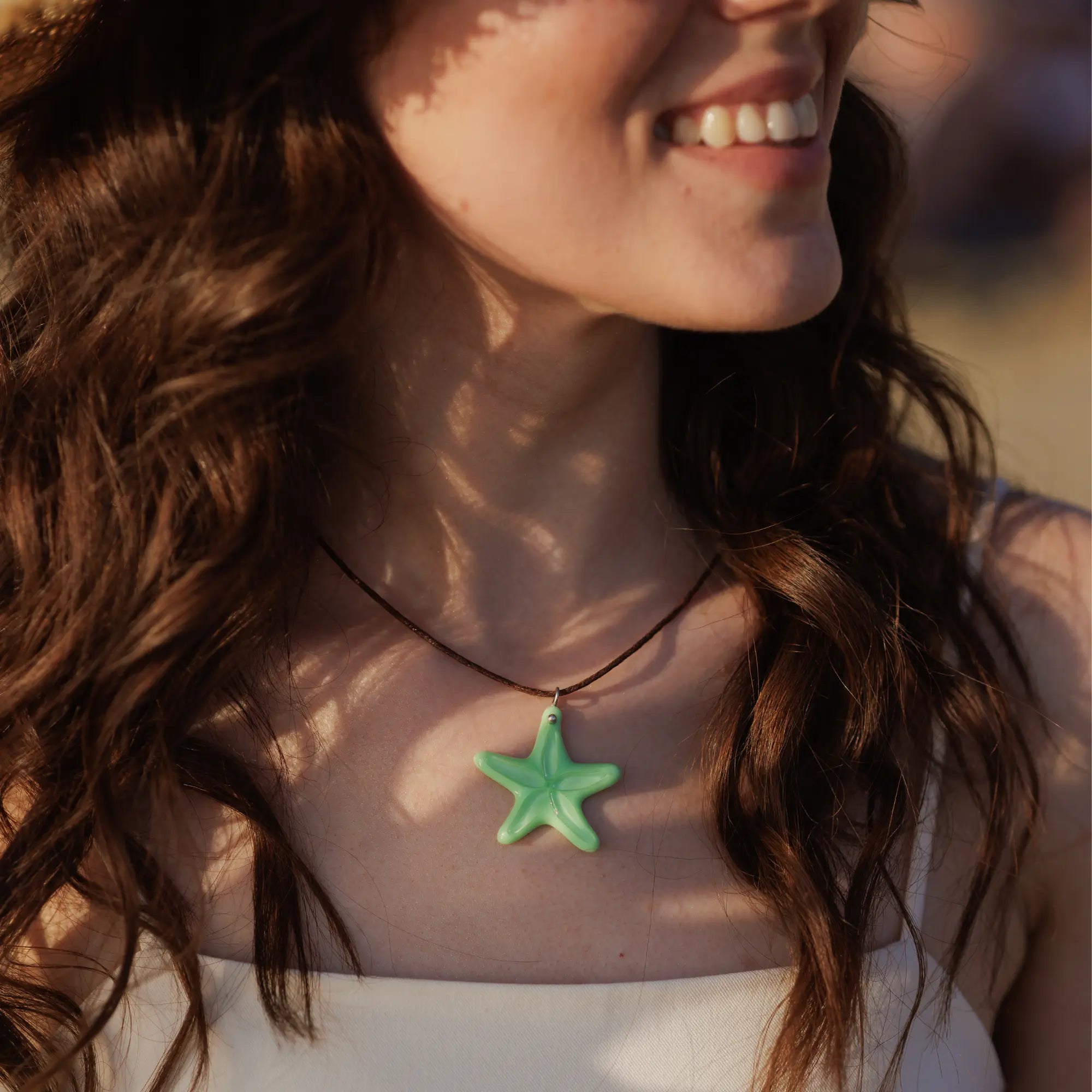 Mint-colored starfish pendant on a brown cord, shown on a woman with long brunette hair and sun-kissed smile.