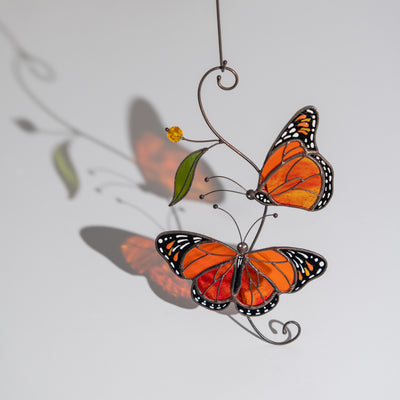 Stained glass monarch butterfly pair casting vivid shadows on the wall, sunlight emphasizing their bright colors.