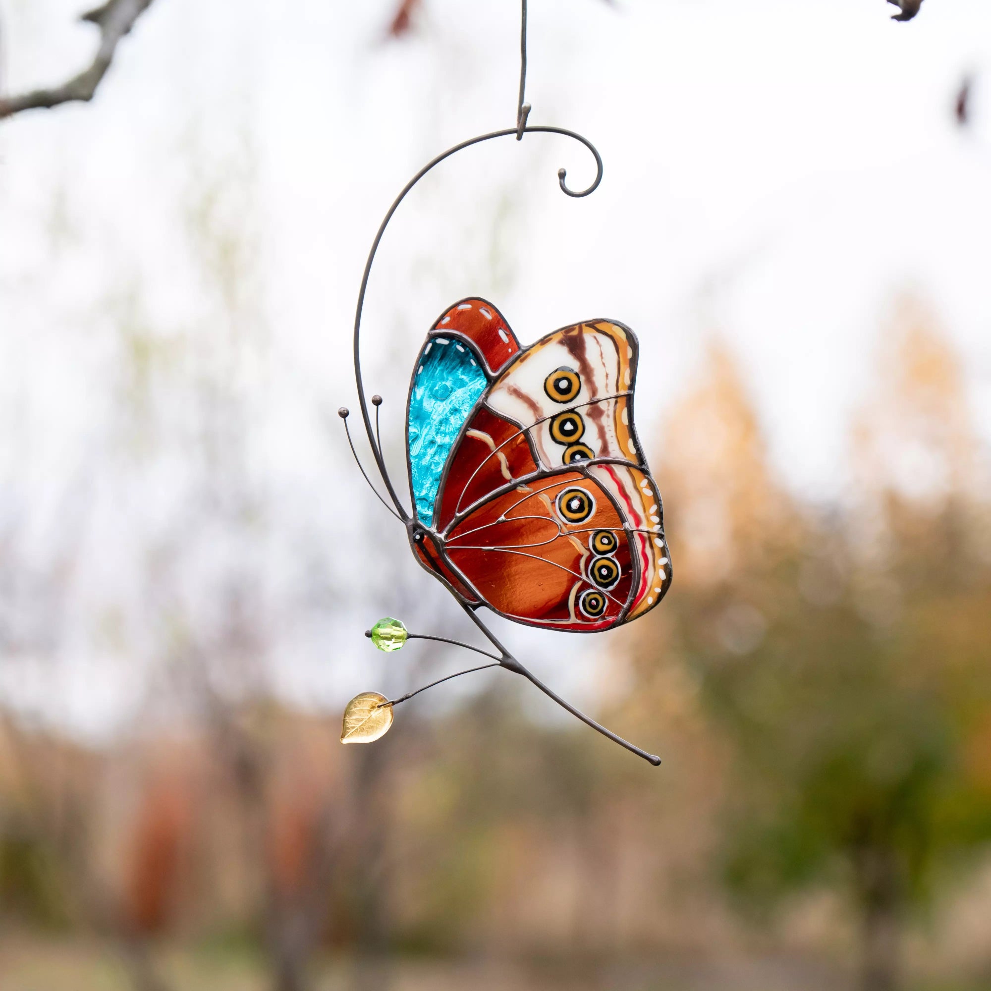 Stained glass butterfly with patterned wings hanging outdoors with soft background