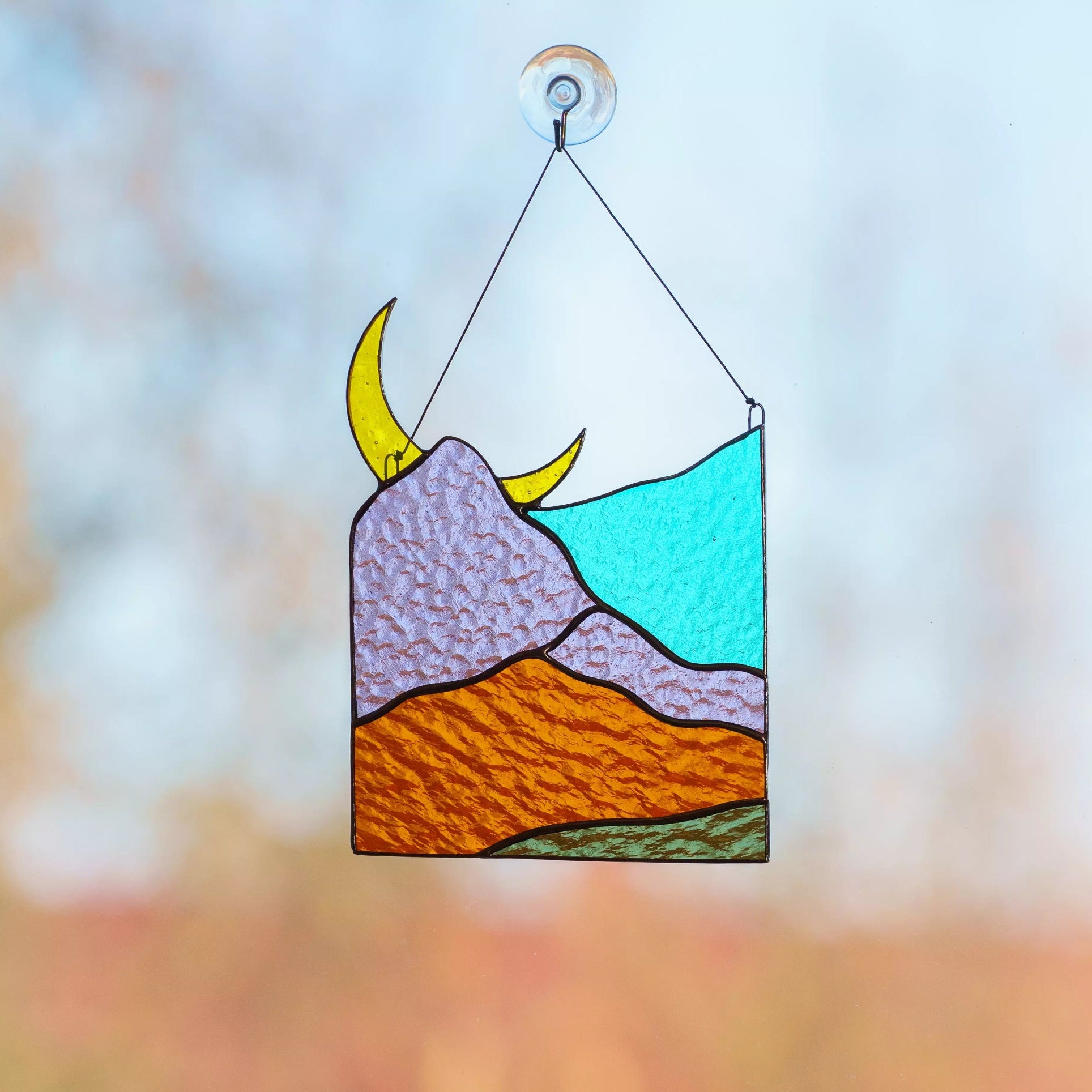 A vibrant mountain landscape stained glass suncatcher hanging against a bright, clear blue sky.