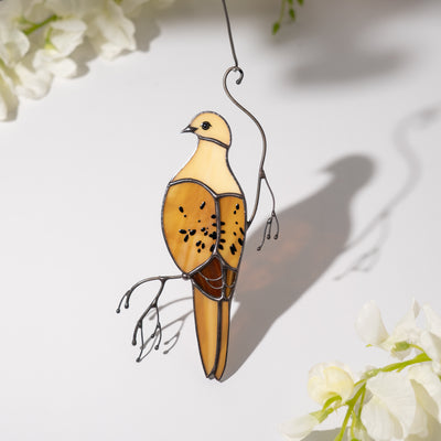 Soft-lit dove suncatcher casting shadow on white table with white flowers nearby.