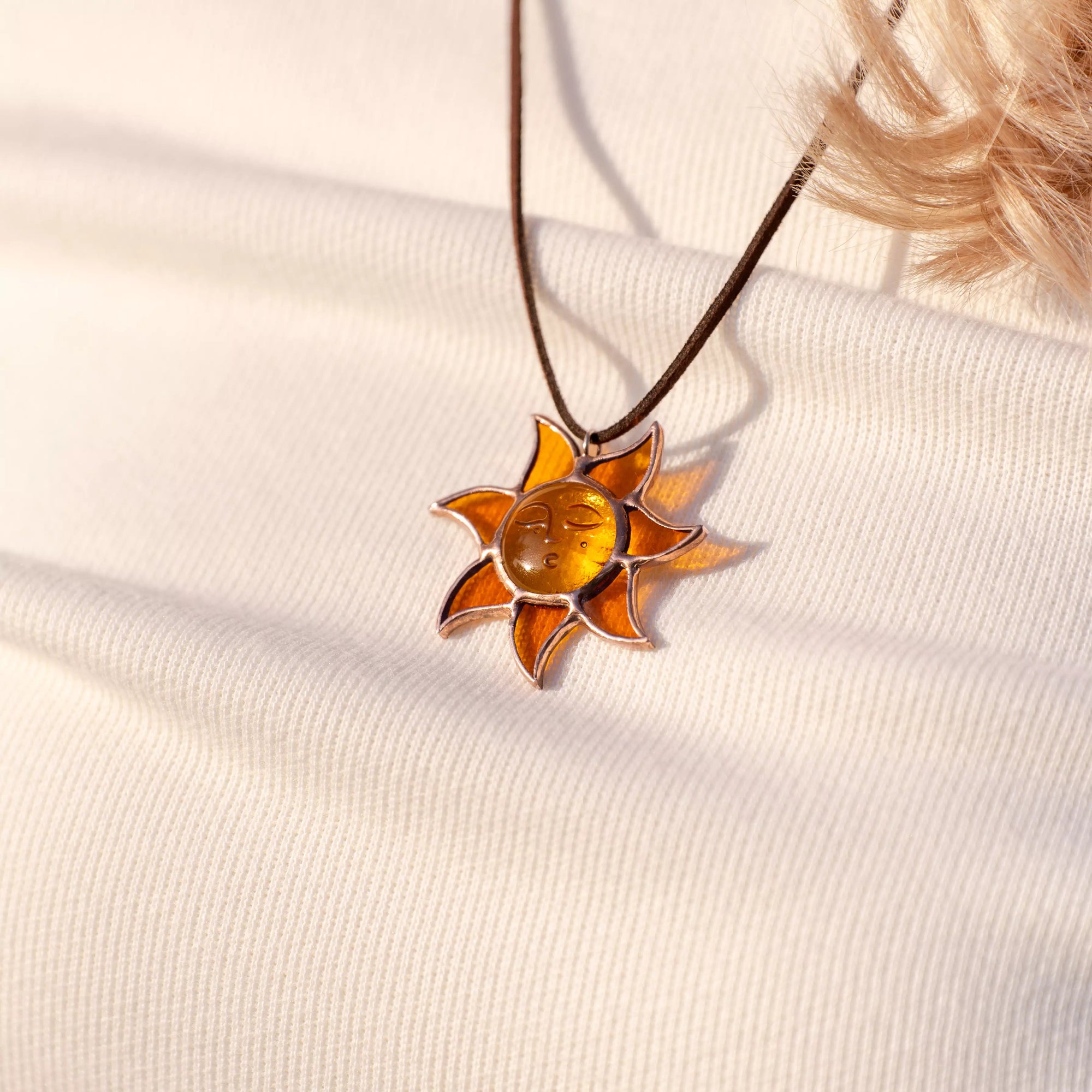 Close-up of amber stained glass sun pendant with face detail, resting on textured white sweater