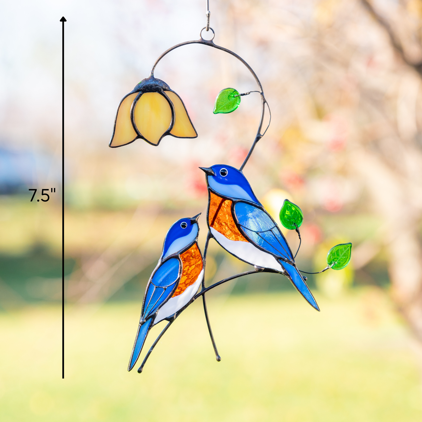 Stained glass suncatcher with two bluebirds, hanging outside in sunlight.