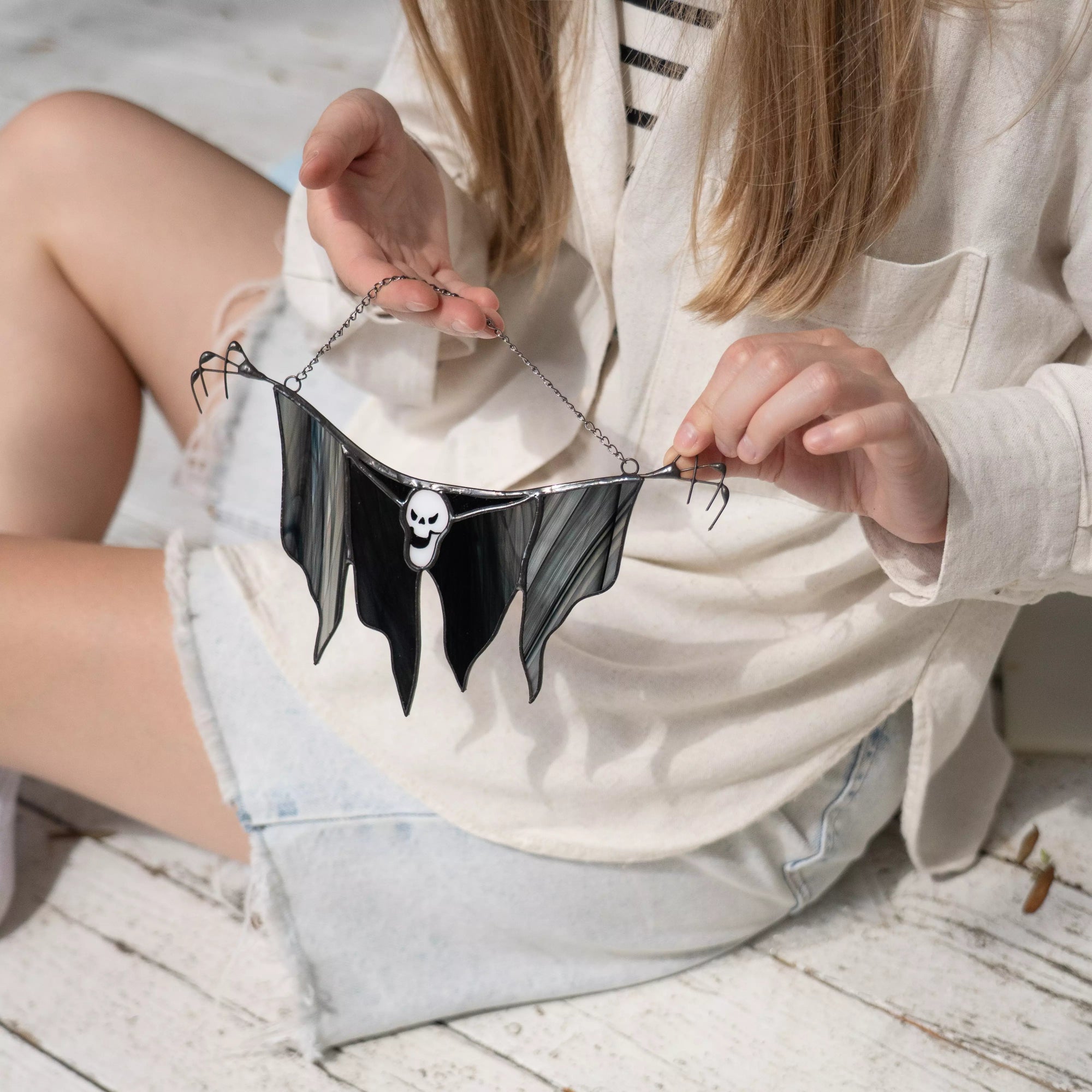 Handholding a black grim reaper with a skull on a light wooden floor.