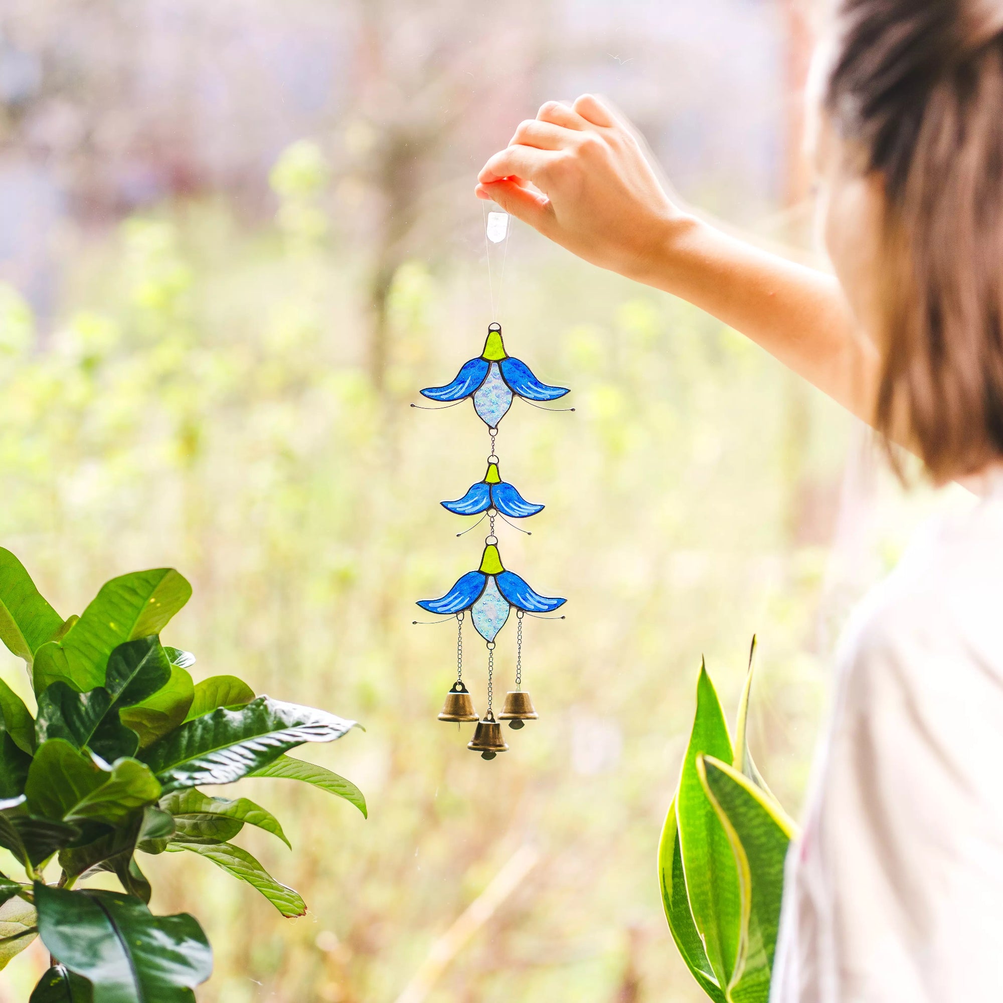 Person holding a blue and green stained glass wind chime with a blurred natural background