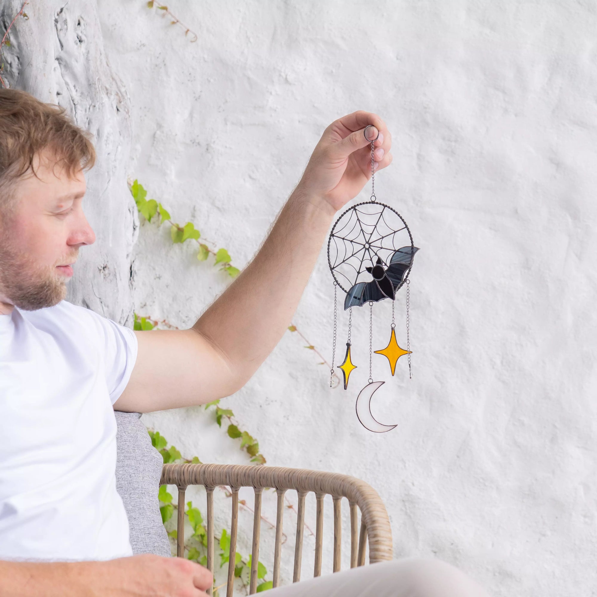 Person holding stained glass bat dreamcatcher wall hanging with a bat design against a white wall.