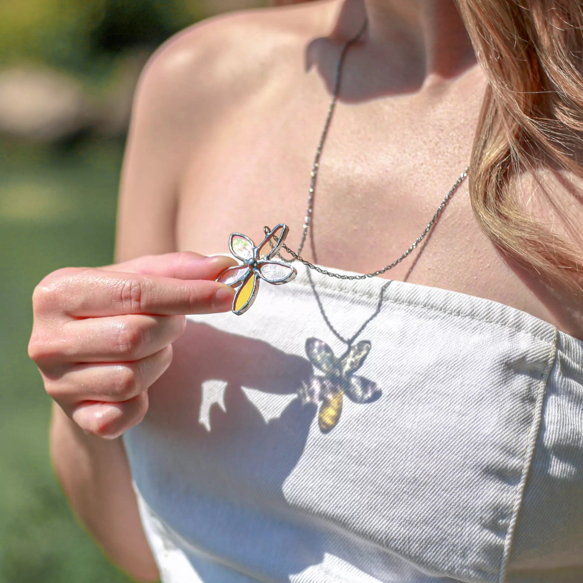 Person holding a flower-shaped stained glass pendant with a blurred natural background