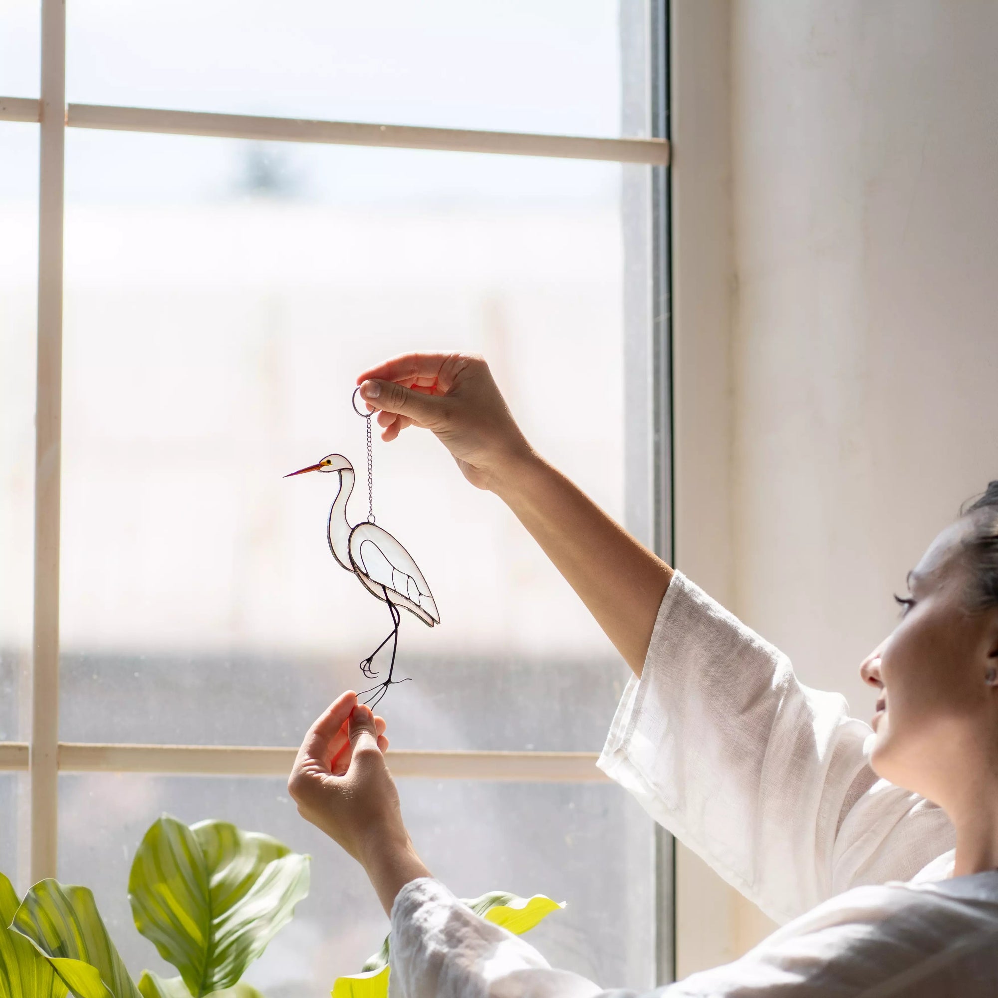 Person holding stained glass heron decoration in front of a window
