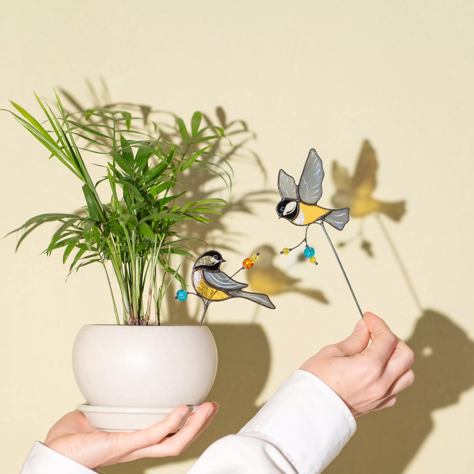 Person holding a potted plant with stained glass chickadee figurines on a beige background