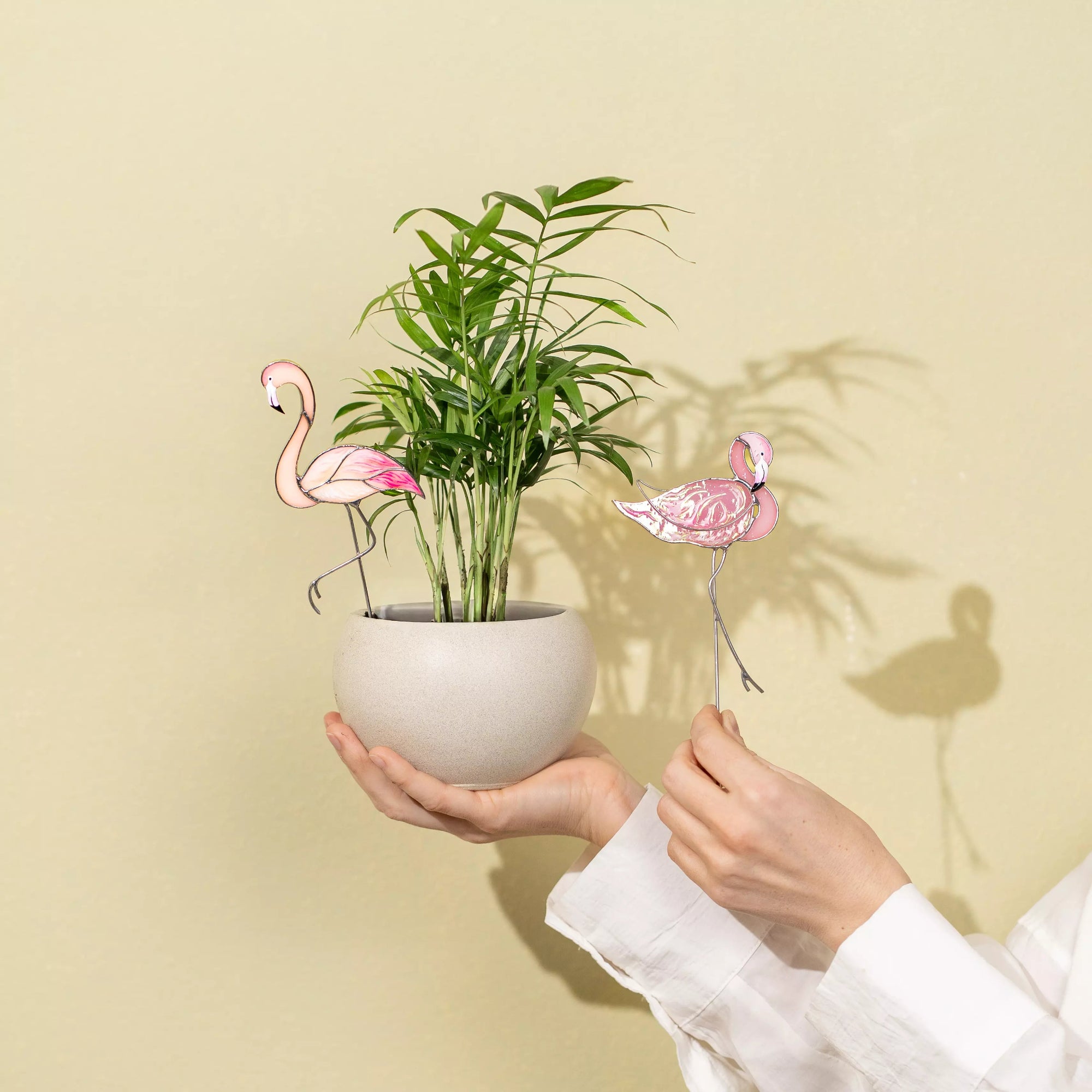 Person holding a potted plant with flamingo stakes against a beige wall