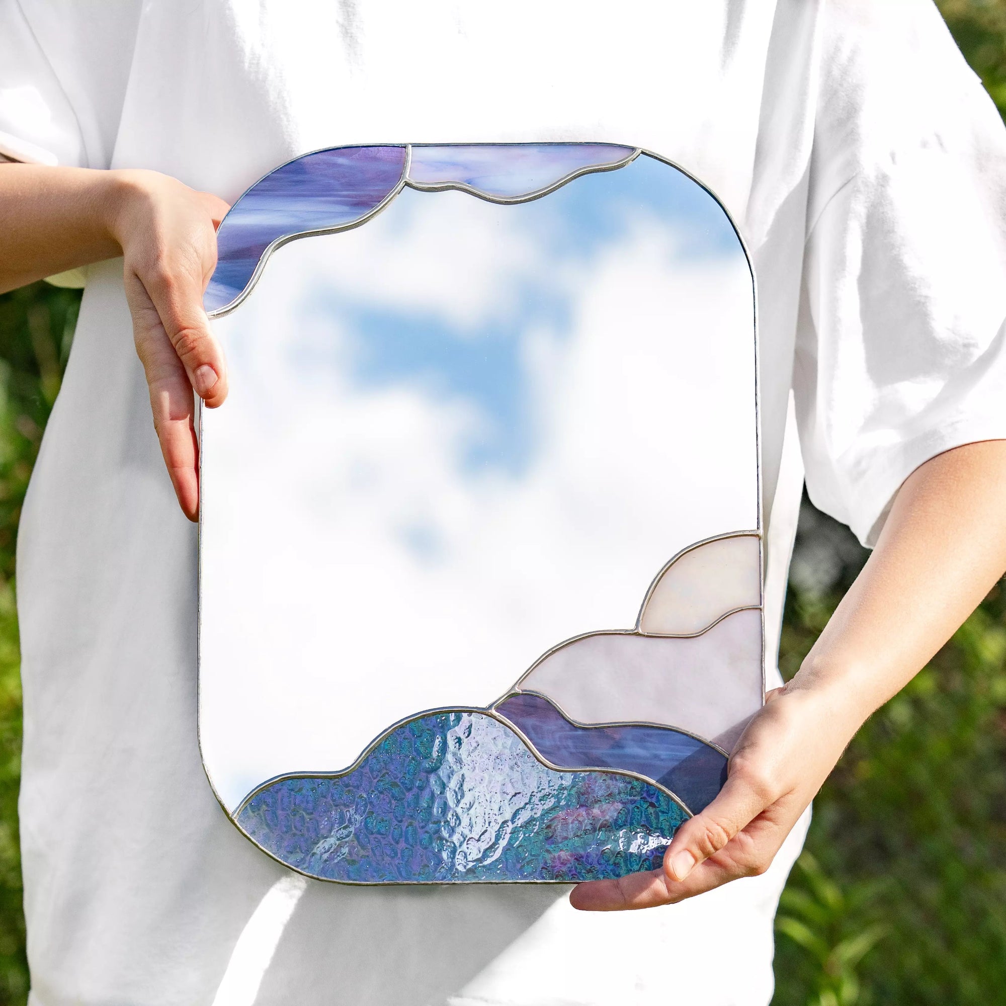 Person holding stained glass mirror with a cloud design against a natural background