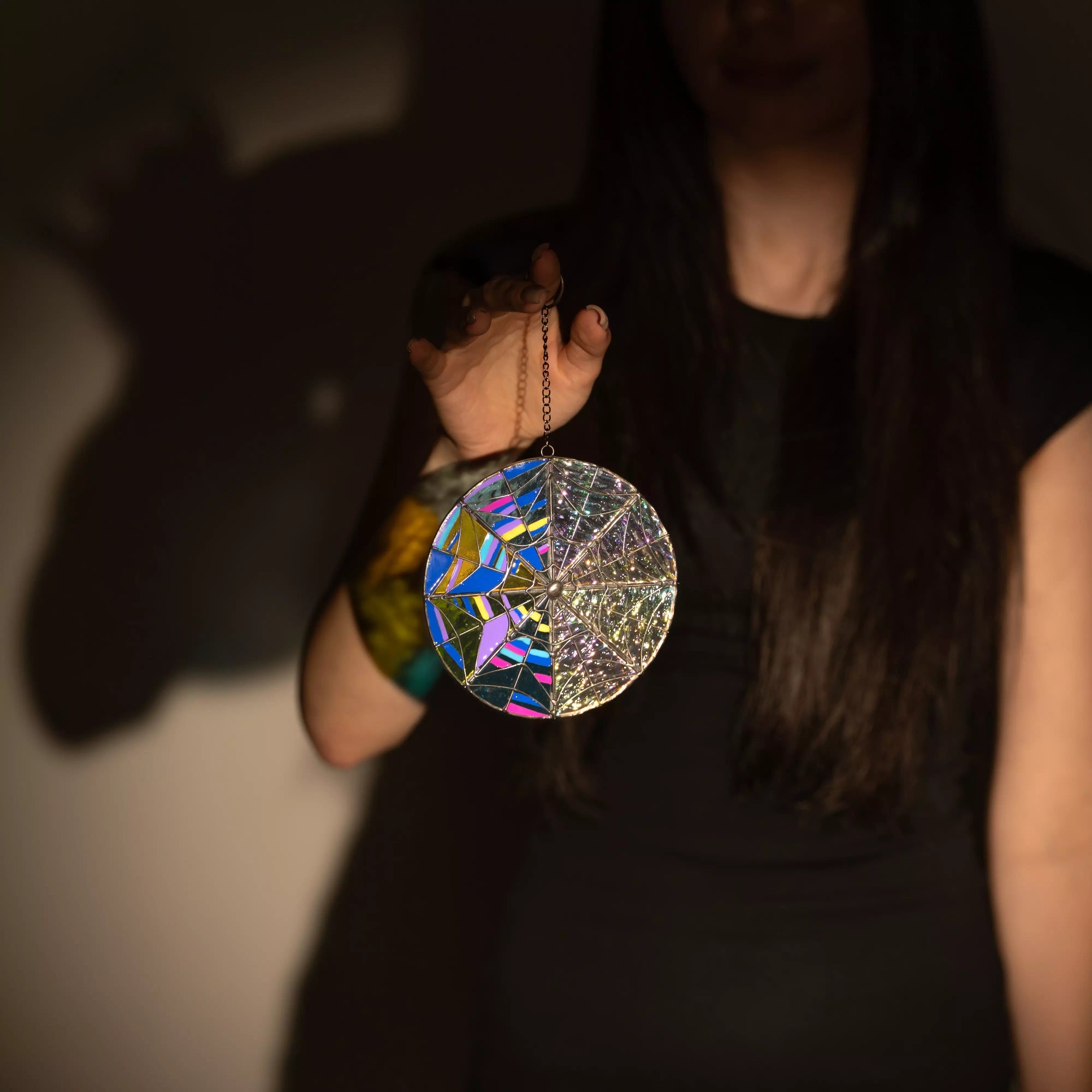 Geometric stained glass round suncatcher held in hand against dark wall