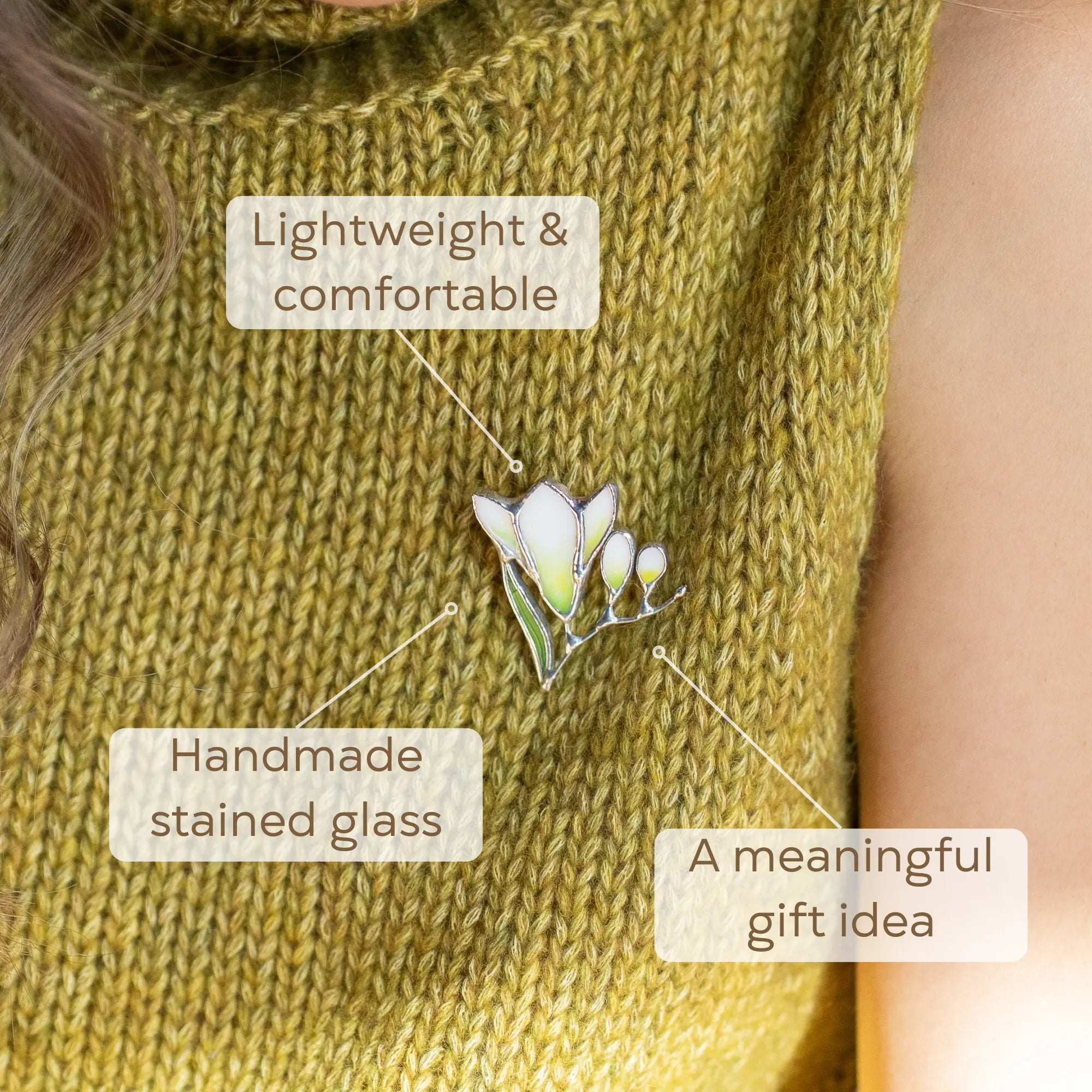 Women wearing a green knitted garment with a stained glass freesia brooch, presented as a meaningful gift idea