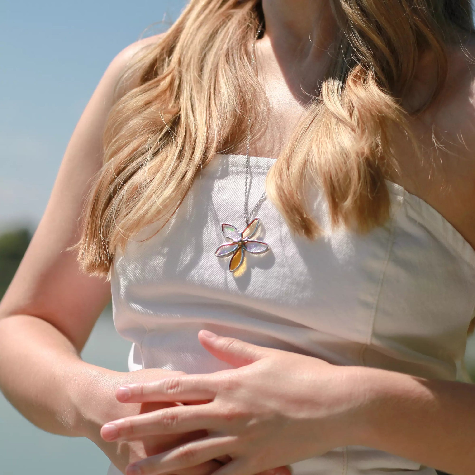 Person wearing a white sleeveless top with a floral stained glass necklace, standing outdoors.