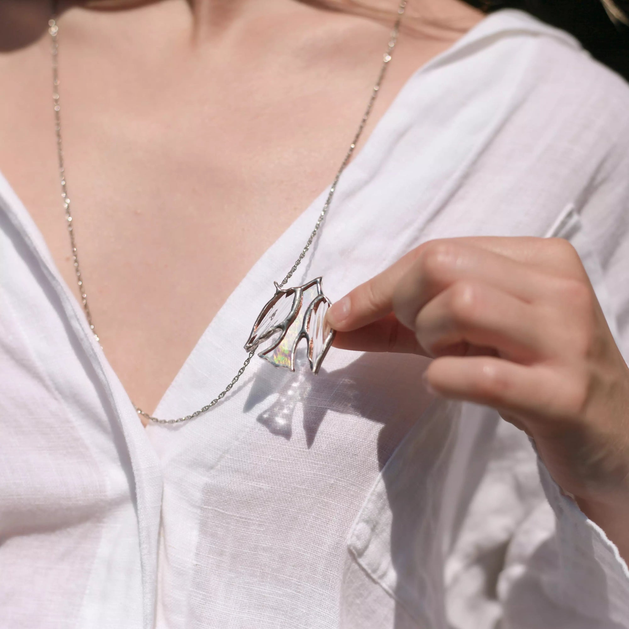 Person wearing a white shirt with a stained glass bird necklace