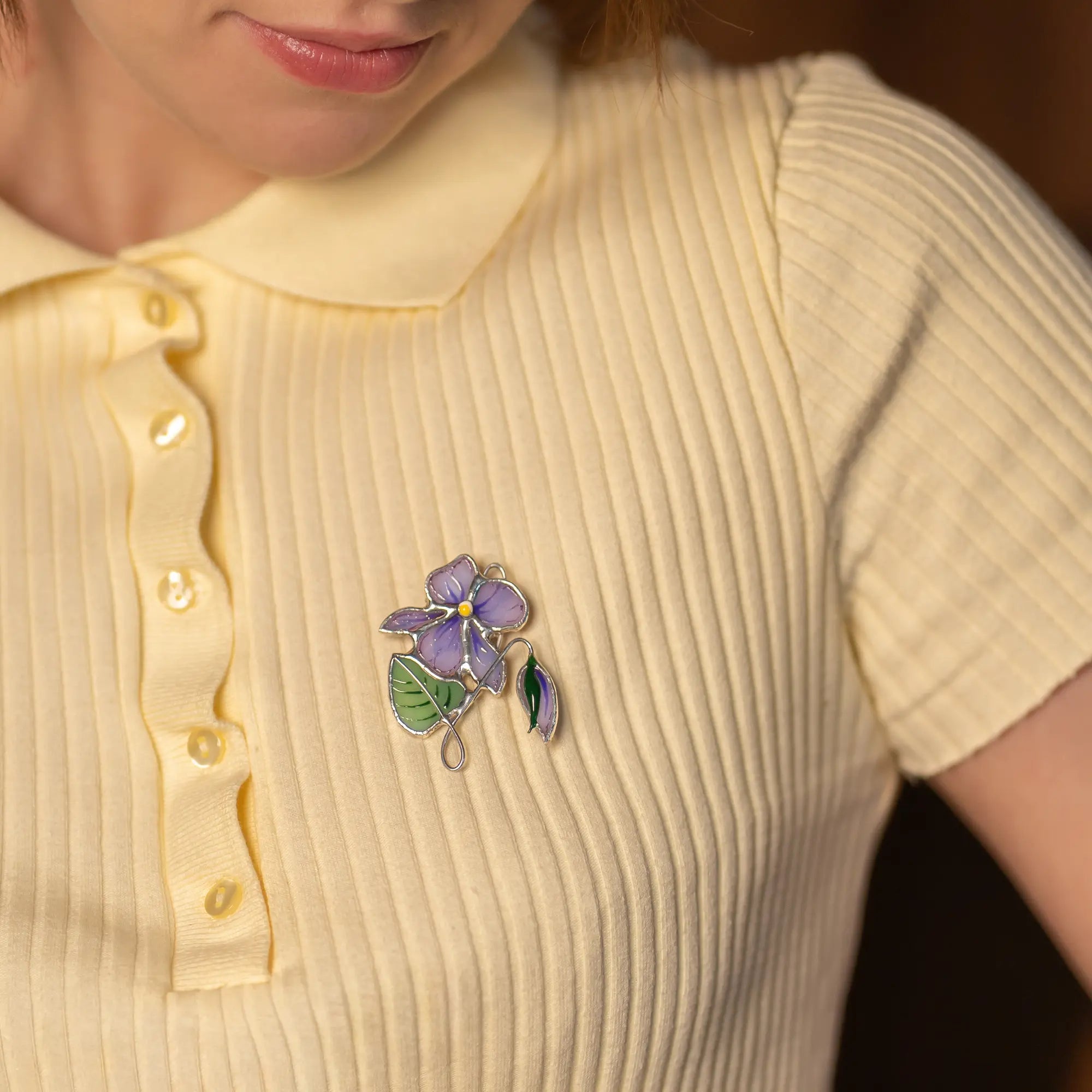 Women wearing a yellow ribbed sweater with a decorative brooch on a dark background