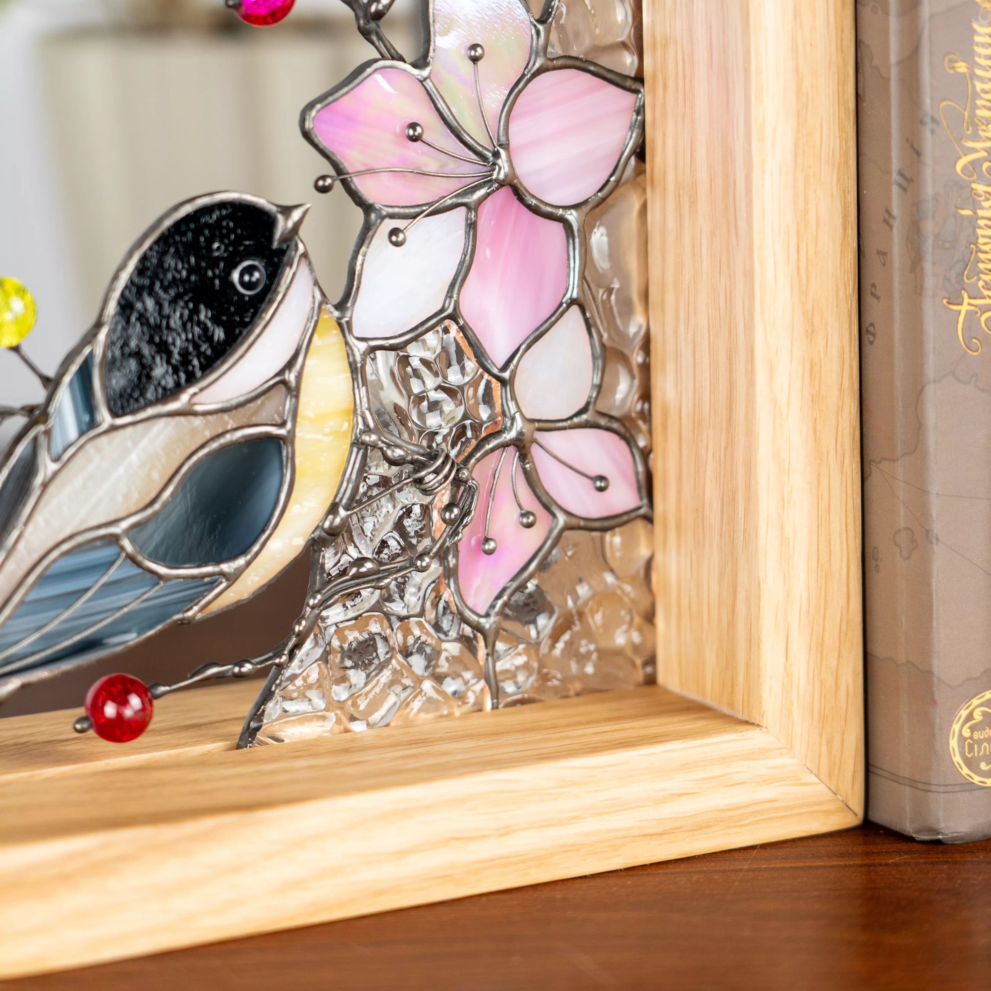 Detailed view of stained glass flowers with soft pink petals, metal solder lines, clear textured glass background, and wooden bookend frame.