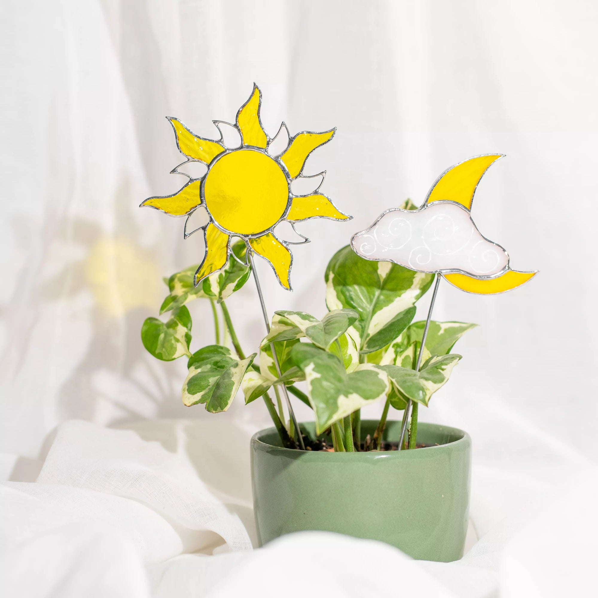 Potted plant with stained glass sun and moon stakes on a white background