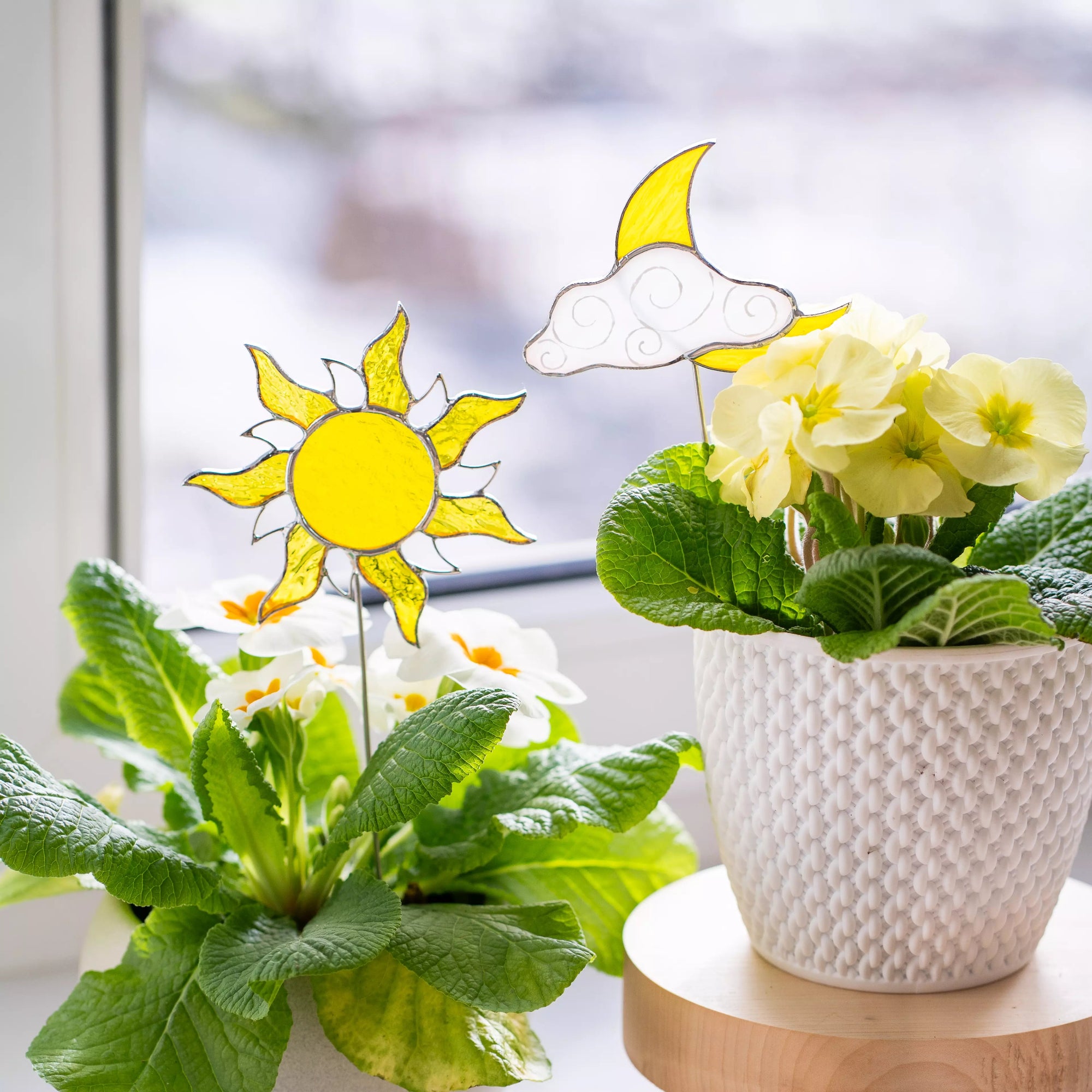 Potted plants with stained glass sun and moon decorations on a windowsill.