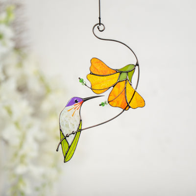 Stained glass hummingbird with clear body and purple head sipping from bright yellow flower
