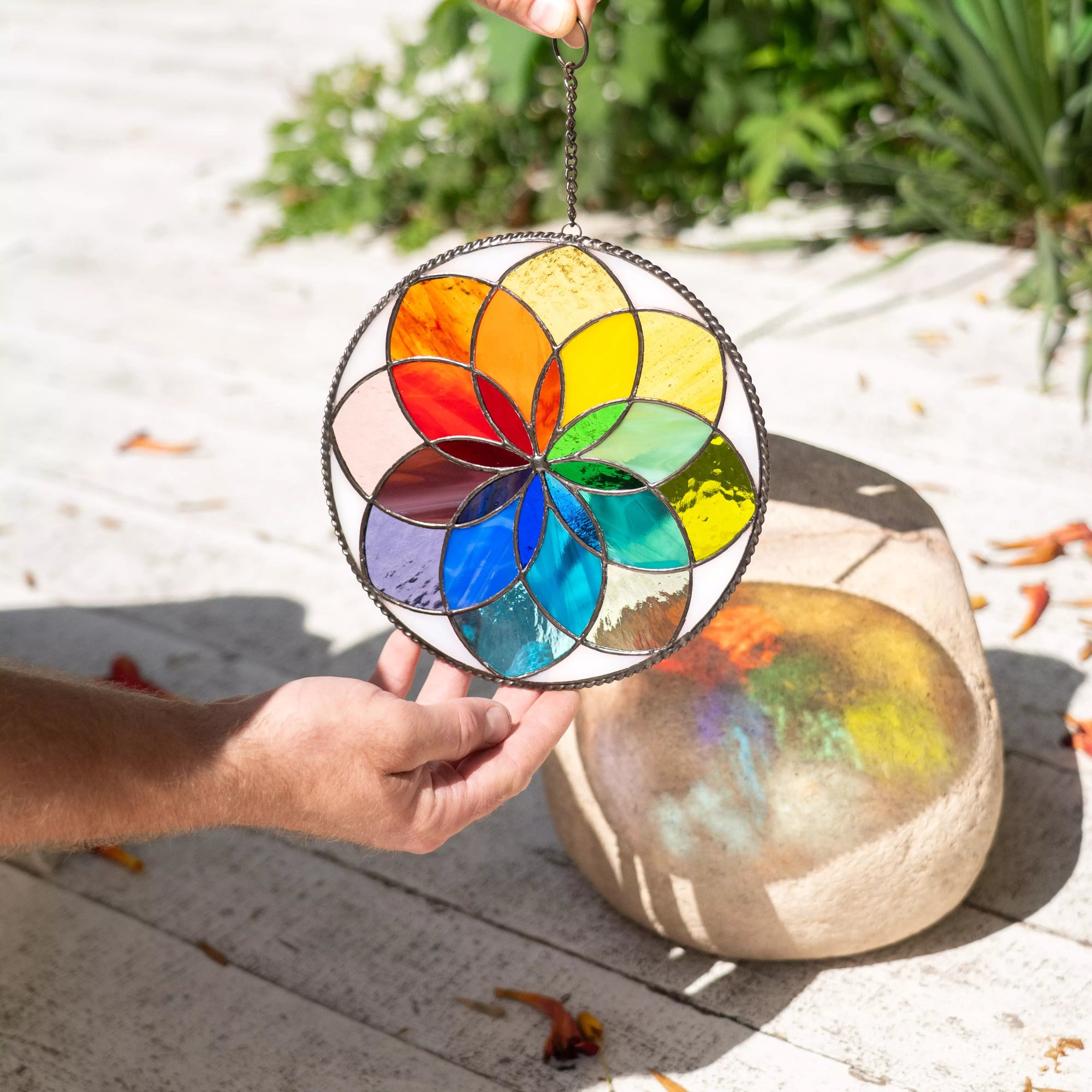 Person holding rainbow stained glass mandala shining reflections in sunlight