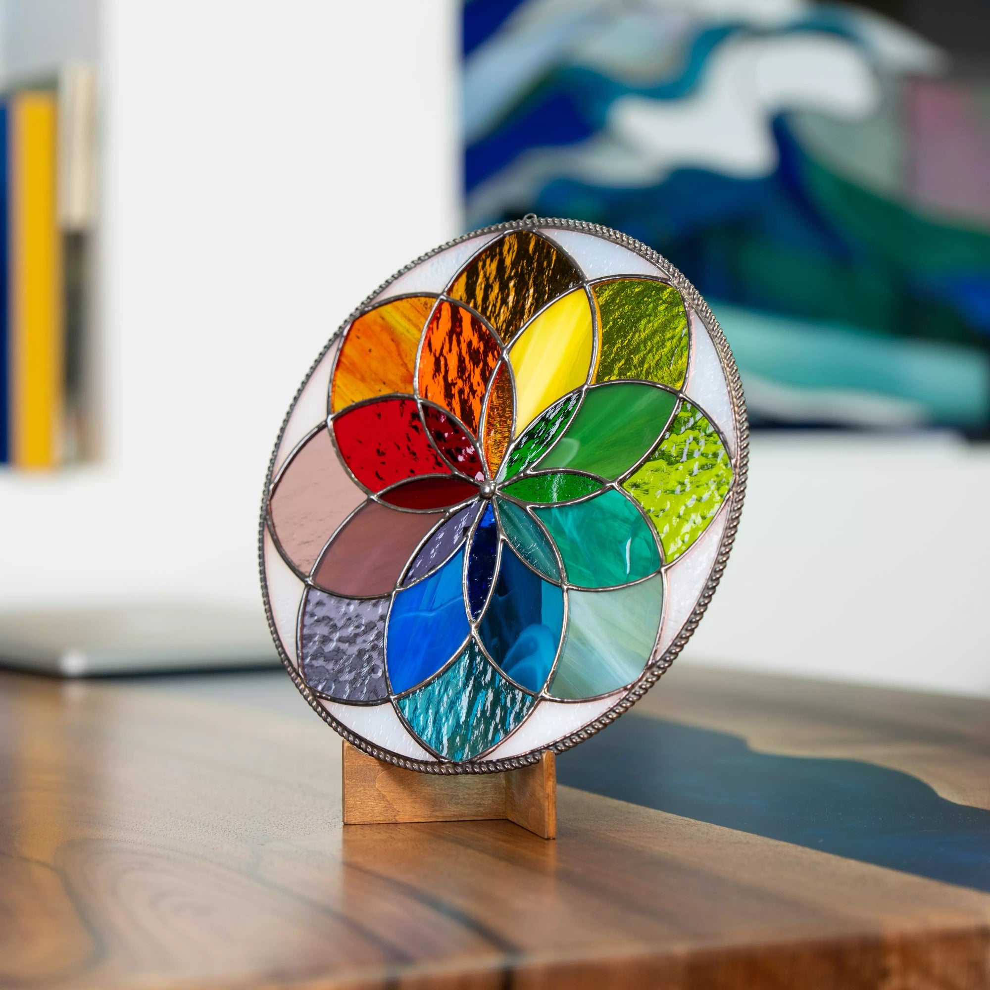 Round stained glass mandala in rainbow colors displayed on wooden base indoors