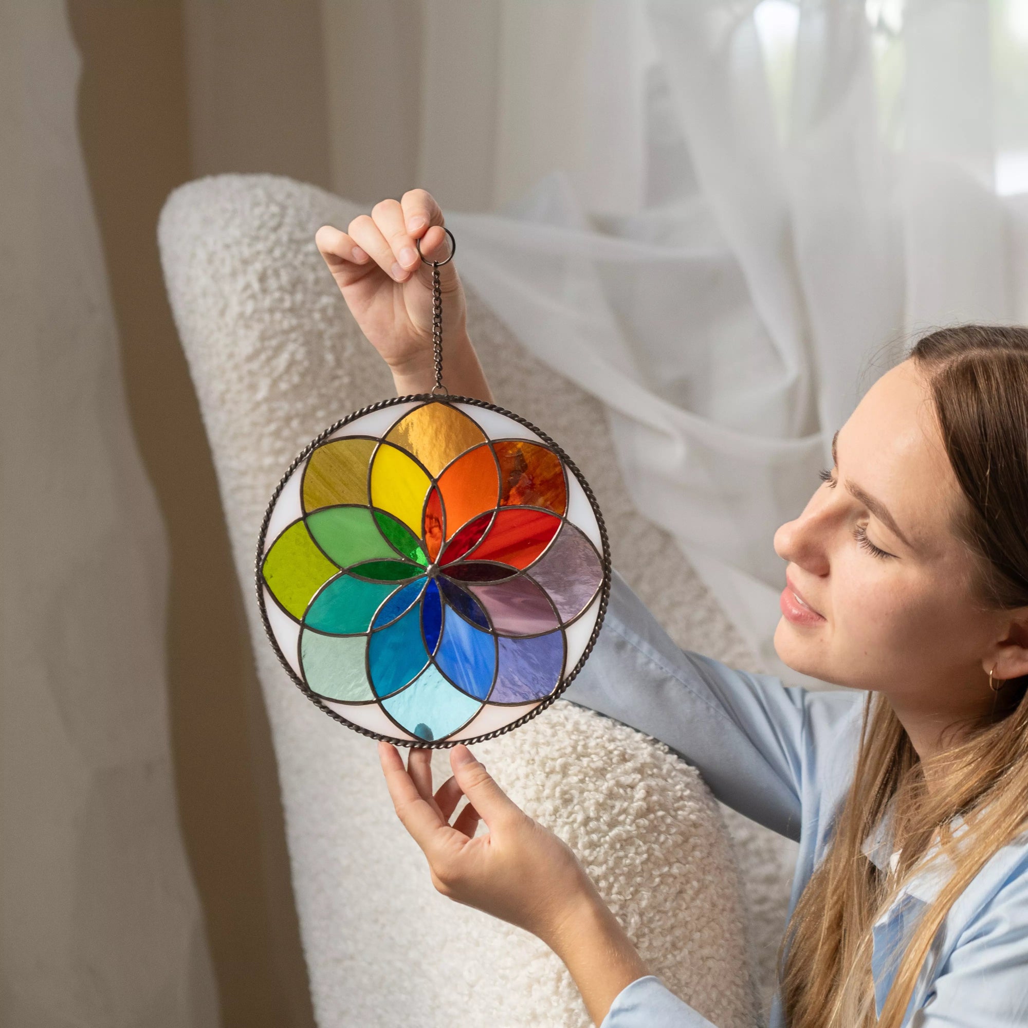 Woman admiring rainbow stained glass mandala with soft light on fabric chair