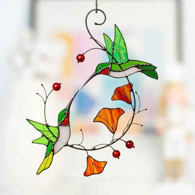 Stained glass hummingbird in green, red, and white flying toward an orange flower