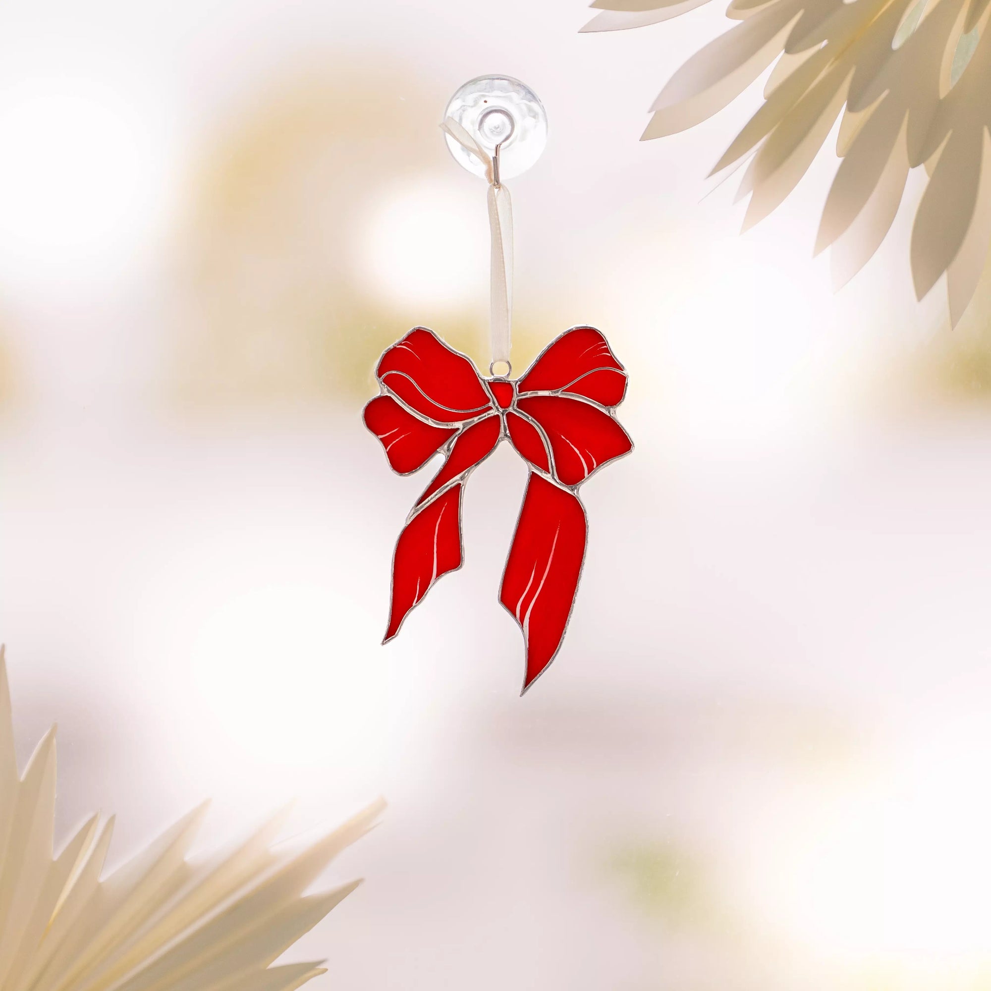 Red bow stained glass suncatcher hanging against a blurred natural background
