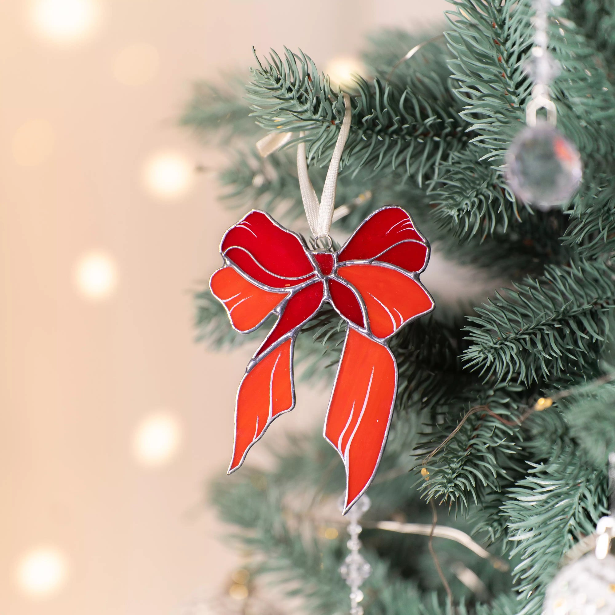 Red bow stained glass ornament on a Christmas tree with blurred lights in the background