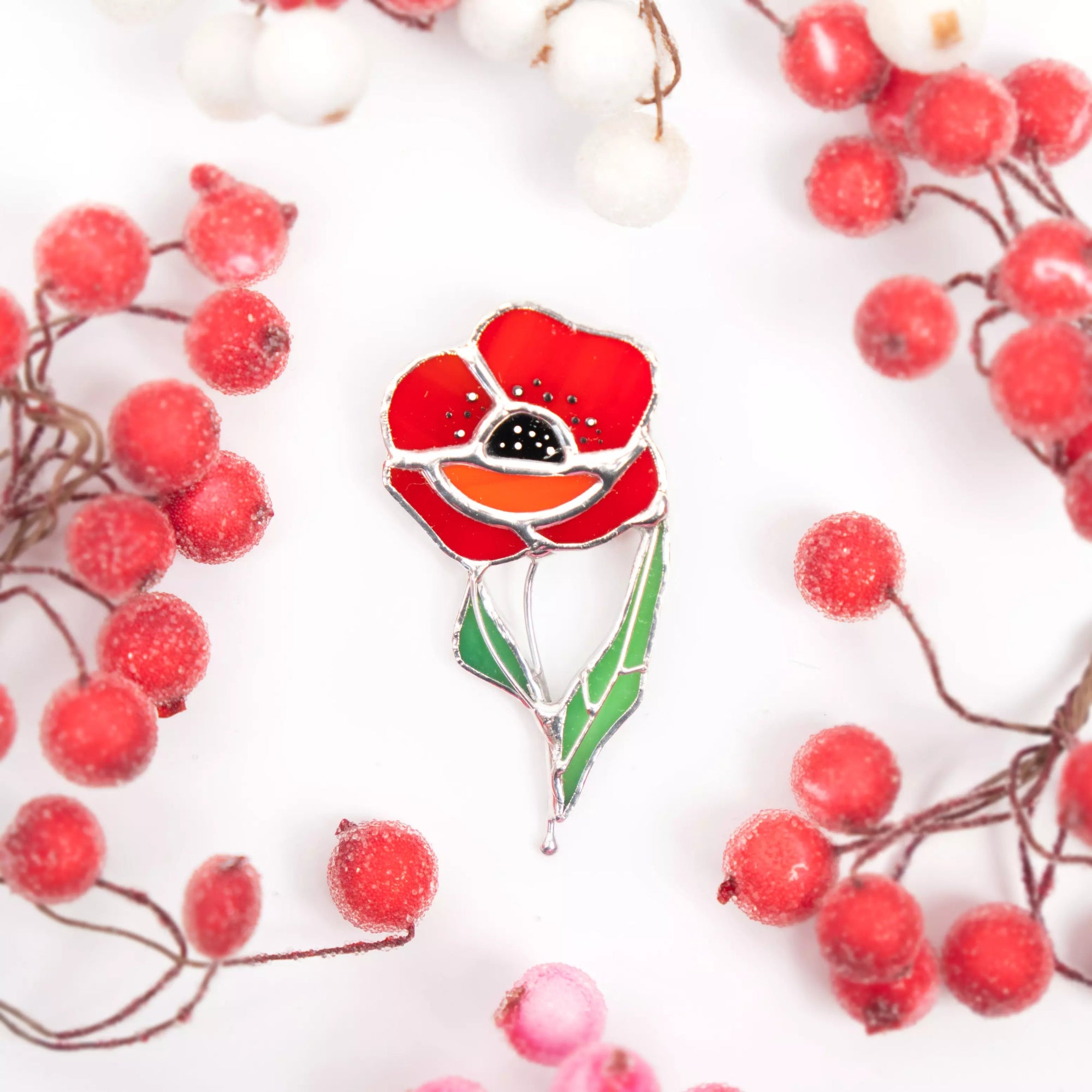 Red poppy stained glass brooch with green stem on a white background with red berries